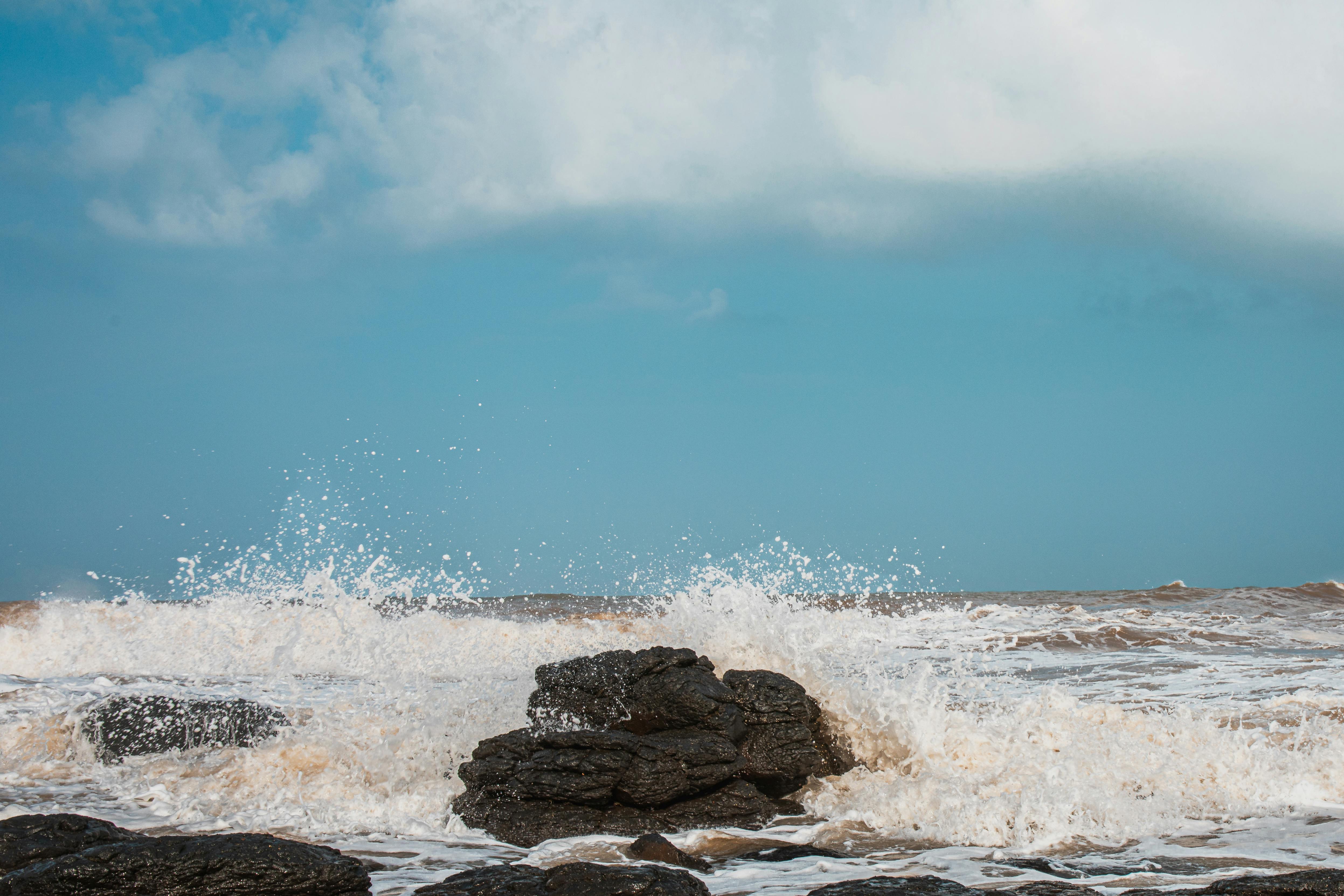 免費 湛藍的天空下，洶湧的波濤拍打著嶙峋的岩石。 圖庫相片