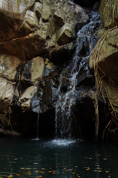 Free Tranquil waterfall cascading over rugged rocks into a calm pool in Ghatshila, India. Perfect for nature and travel themes. Stock Photo