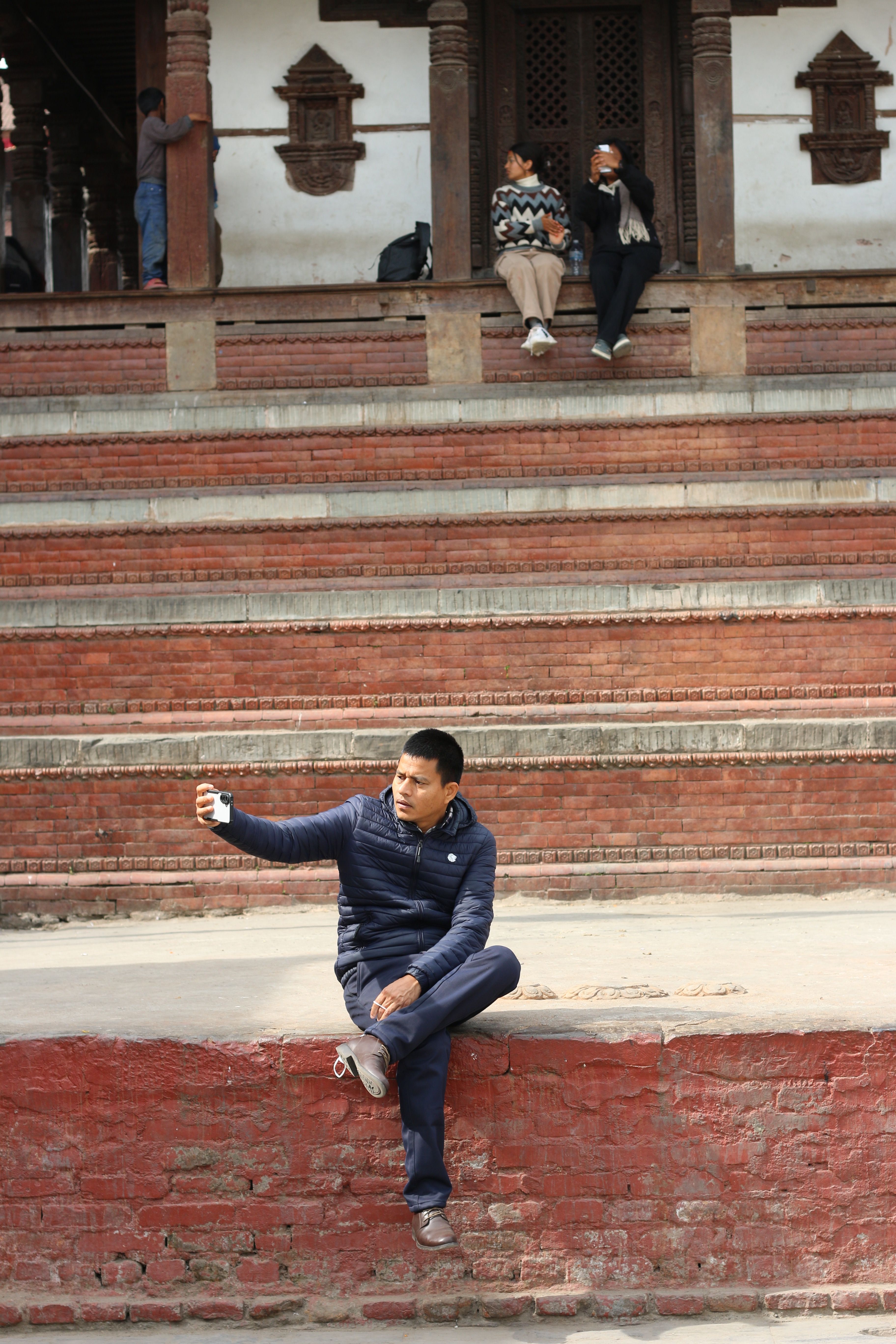A man taking a selfie at Durbar Square, Kathmandu, Nepal with traditional architecture in the background.