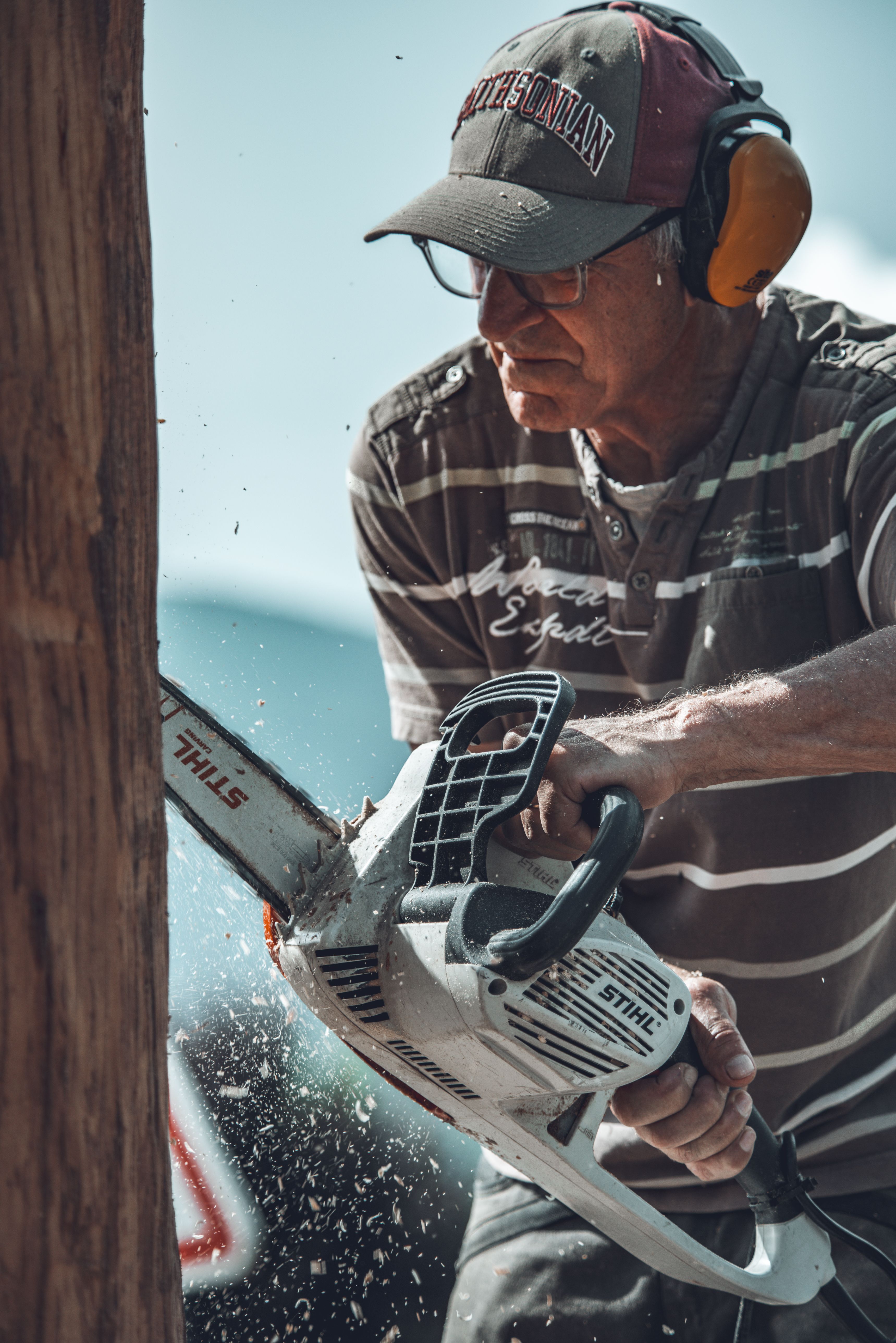 Adult man expertly using a chainsaw to cut wood outdoors during the day.