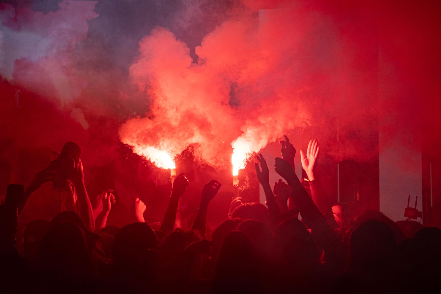 Vibrant scene of a lively crowd celebrating with red flares at night.