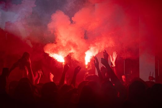 Vibrant scene of a lively crowd celebrating with red flares at night.