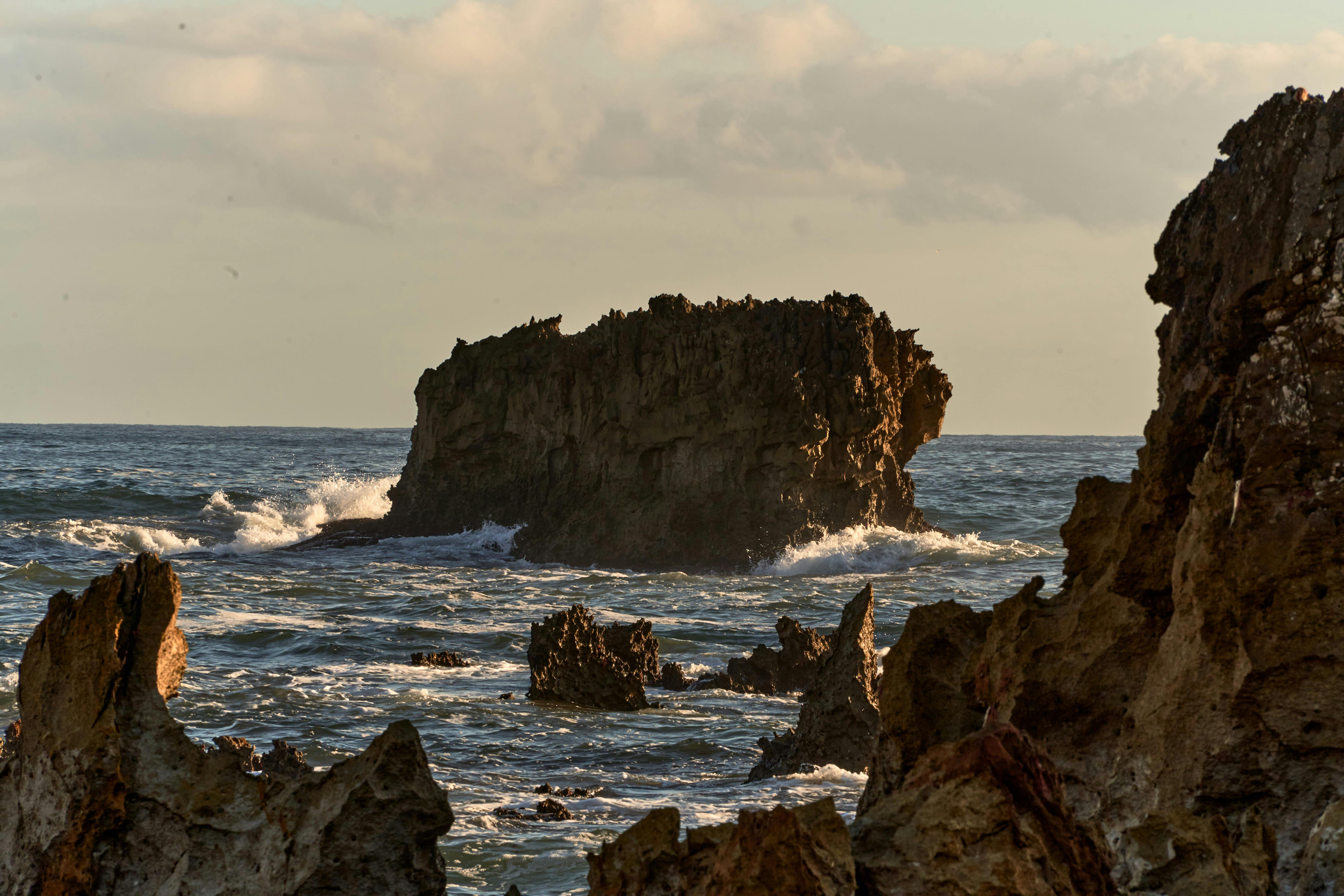 무료 스페인 리바데셀라의 바위투성이 해안선과 부서지는 파도가 석양에 물든 모습. 스톡 사진