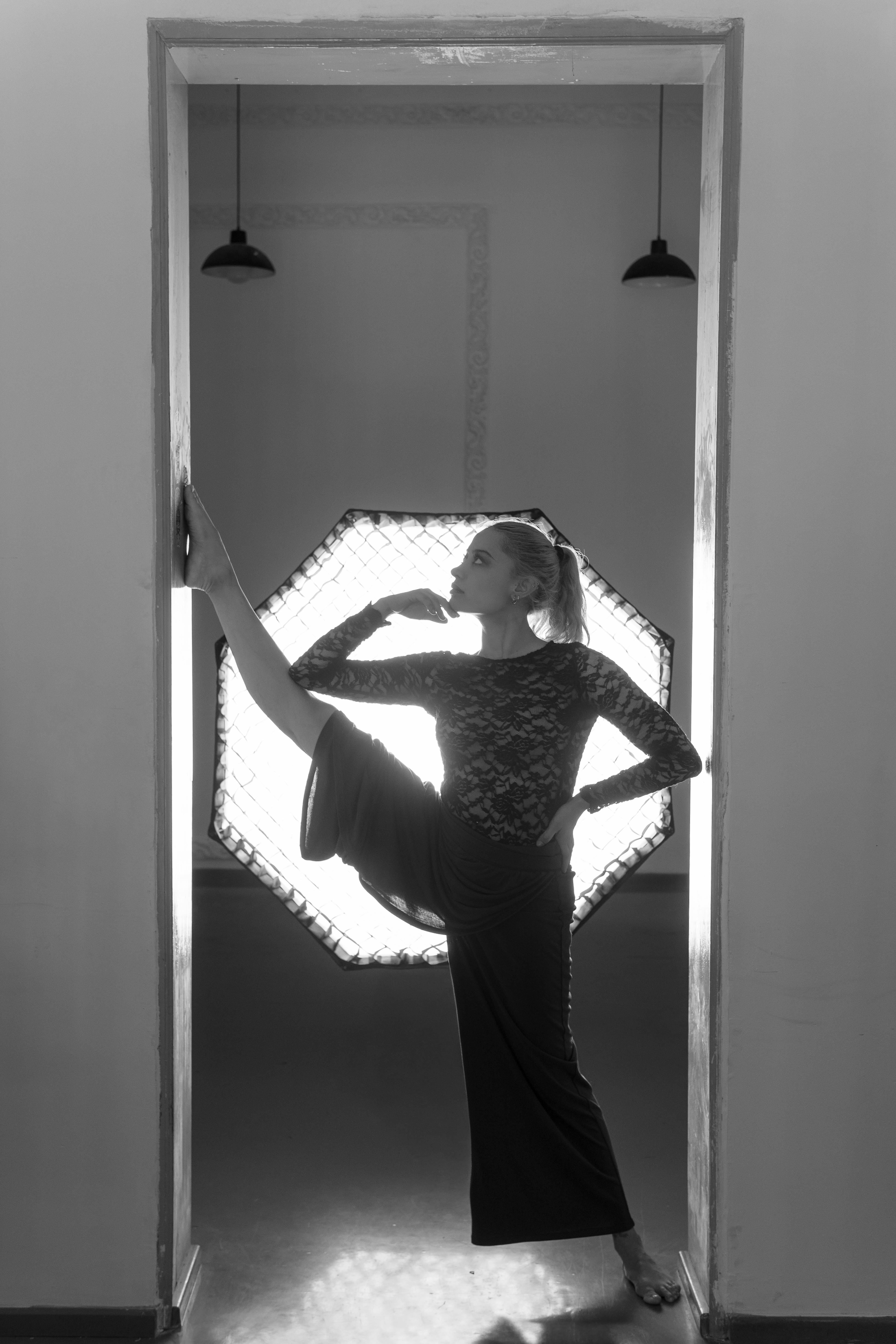 ingyenes Fekete-fehér fotó egy női táncosról, aki kecsesen pózol egy ajtóban, lágy fény háttérrel. Stockfotó