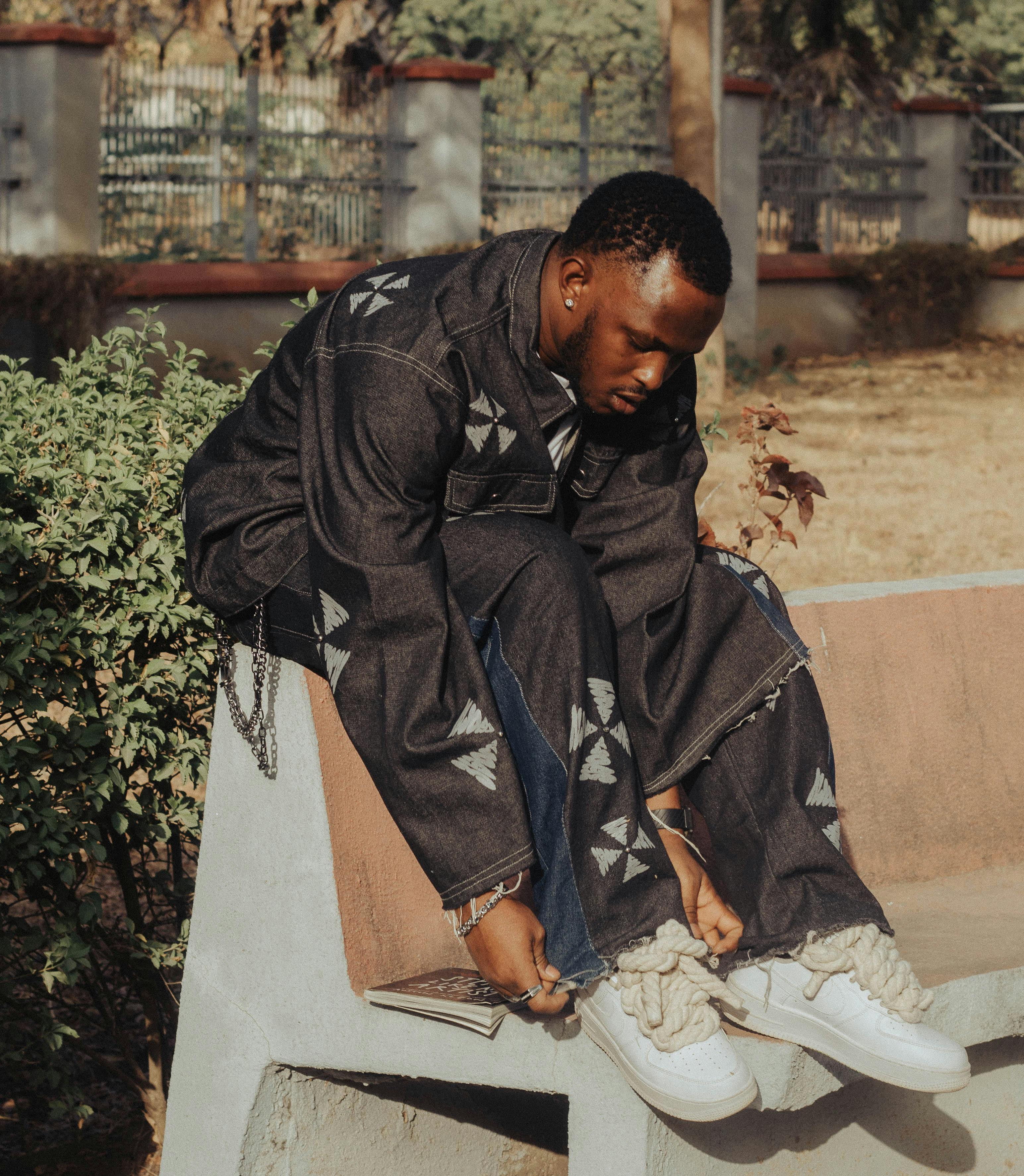 免费 一位身着牛仔服的时尚年轻男子坐在户外的水泥长椅上，正在调整鞋子。 素材图片