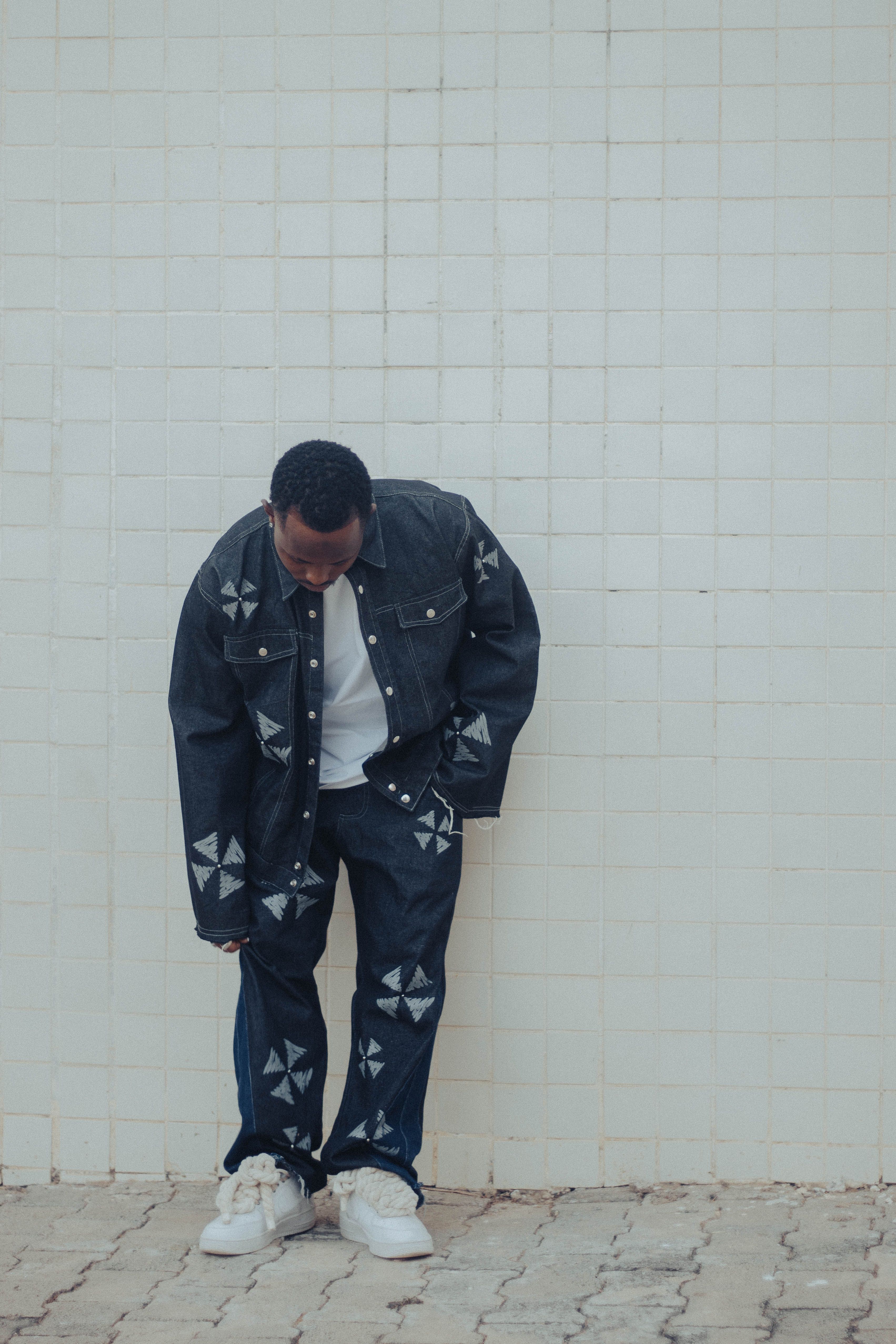 Person in stylish denim outfit leaning against a white tiled wall.