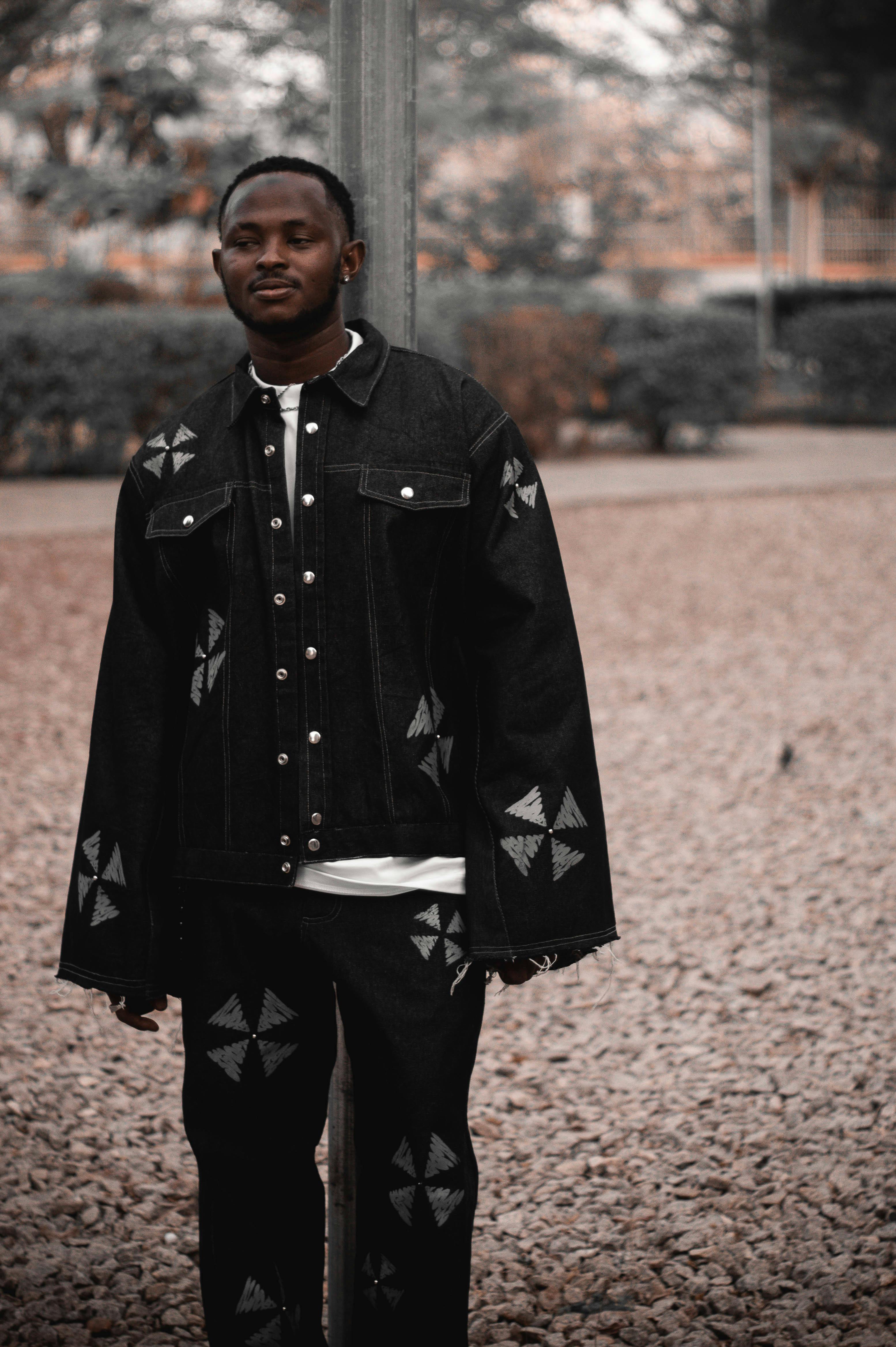 ฟรี ชายคนหนึ่งโพสท่าในชุดเดนิมสีดำสุดแปลกตาในสถานที่กลางแจ้ง คลังภาพถ่าย