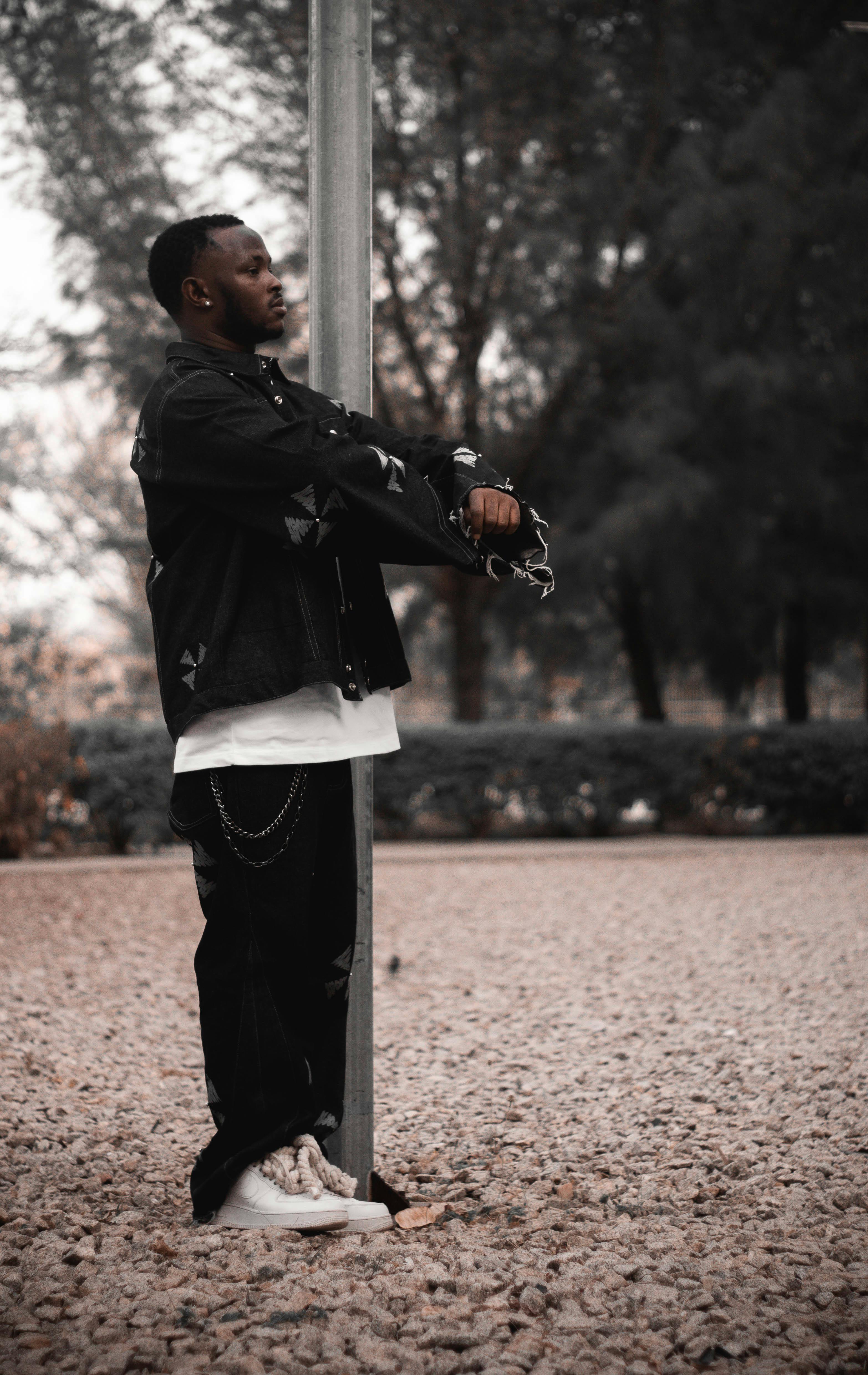 ingyenes Sötét öltözékű fiatalember pózol a szabadban, modern utcai divatot bemutatva. Stockfotó