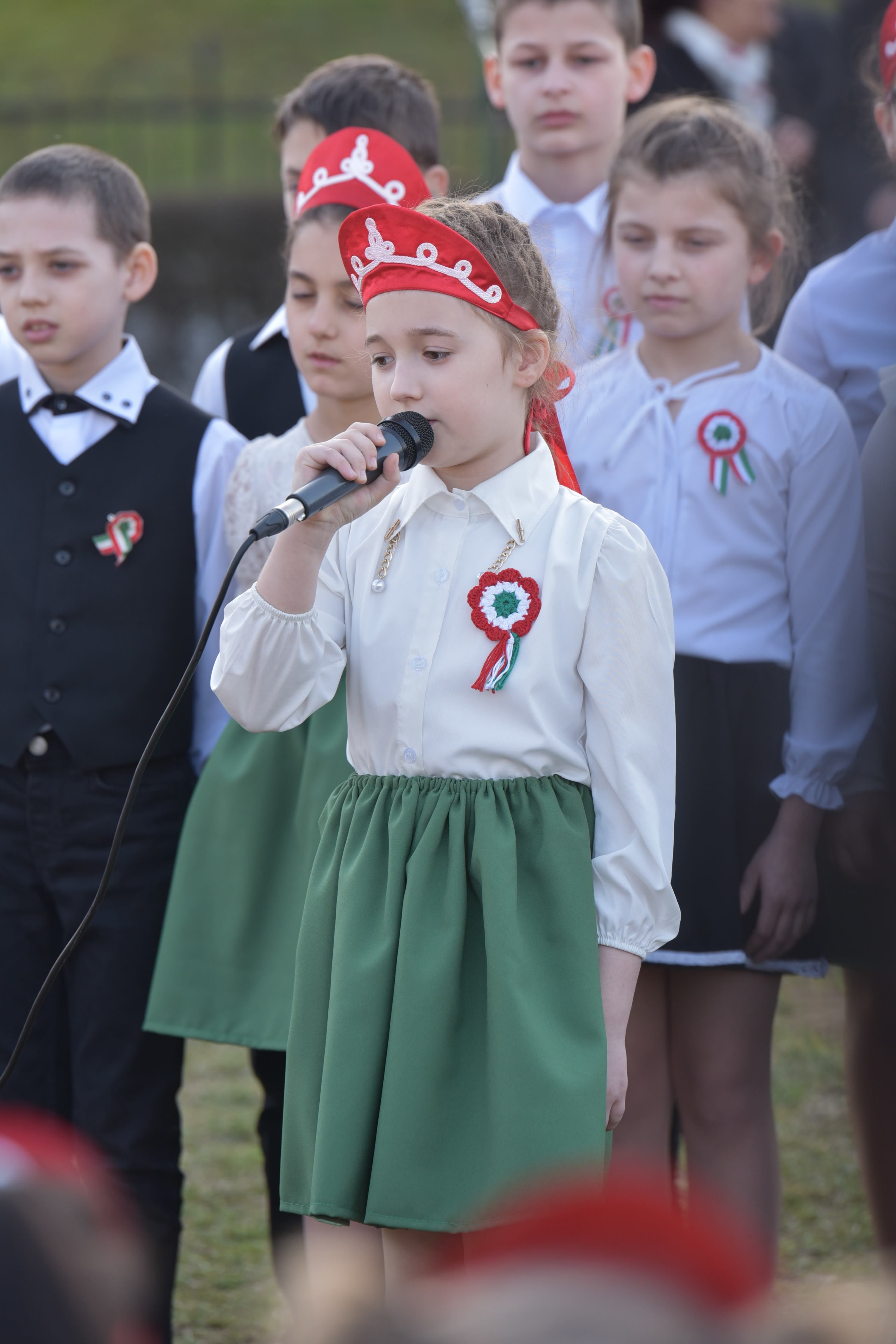 Group of children in traditional attire performing during a national celebration outdoors.