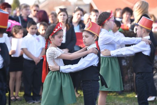 Children in costumes performing a traditional dance at an outdoor event, lively atmosphere.