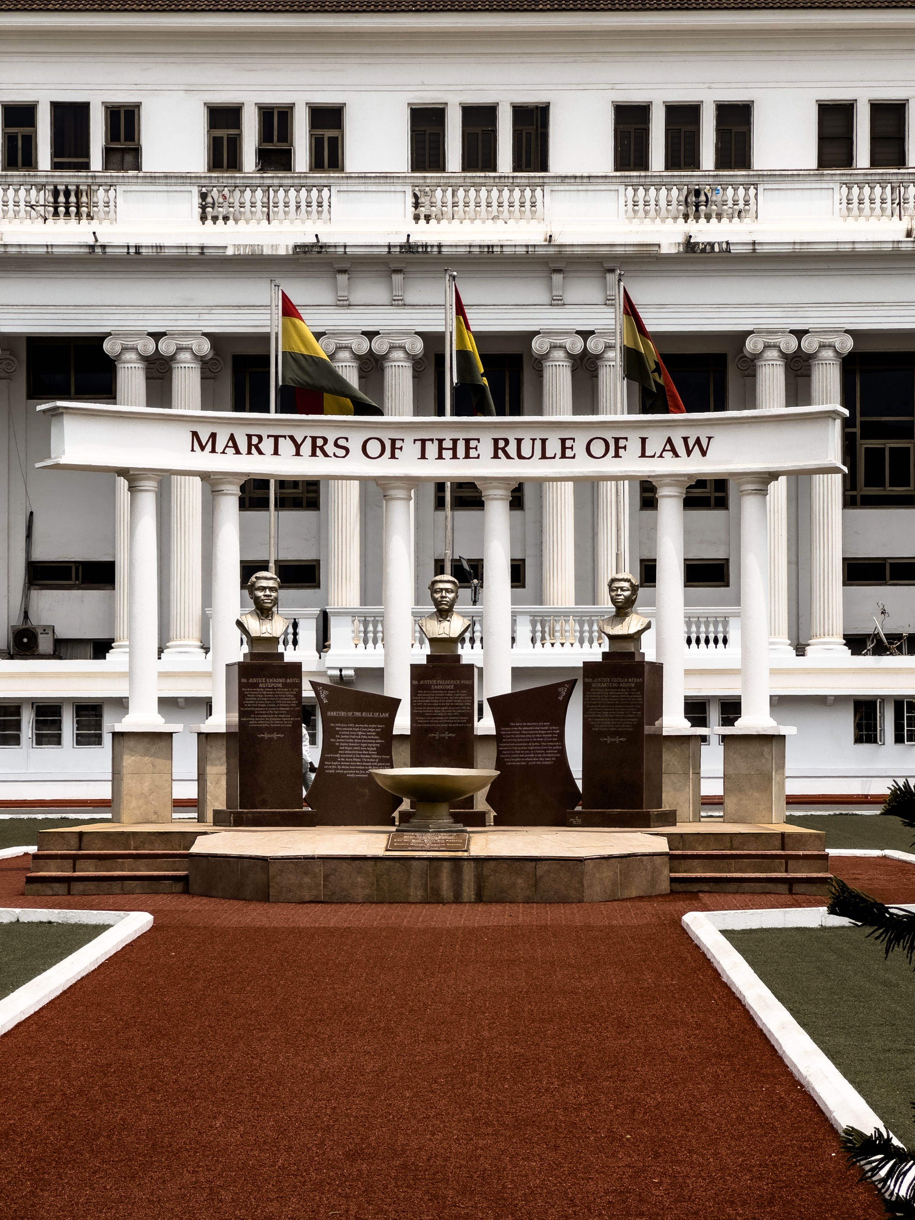 Monument honoring martyrs of the rule of law with statues and flags in front of a historic building.