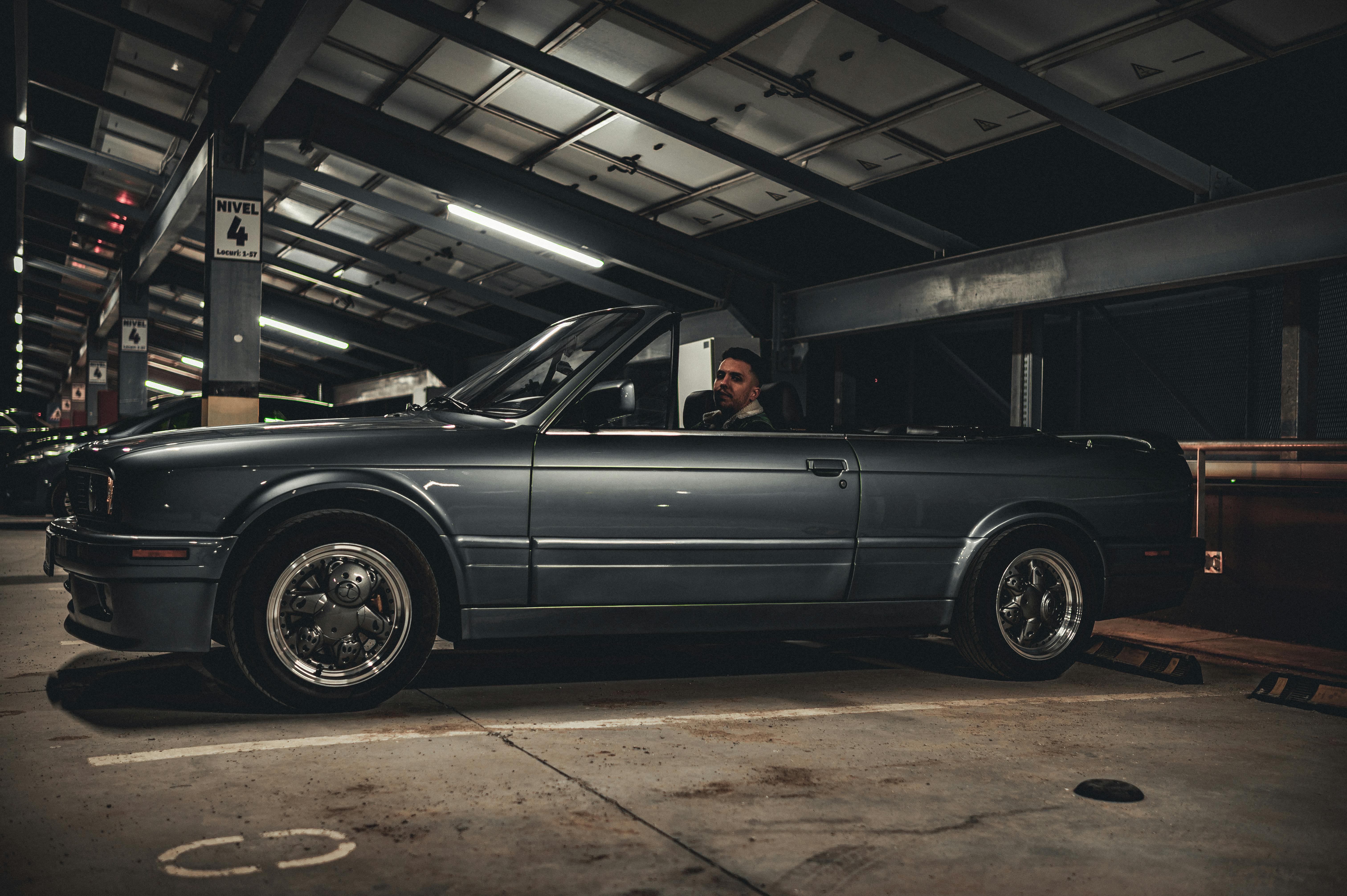 Безкоштовне Чоловік сидить у старовинному кабріолеті, припаркованому в міському гаражі вночі. стокове фото