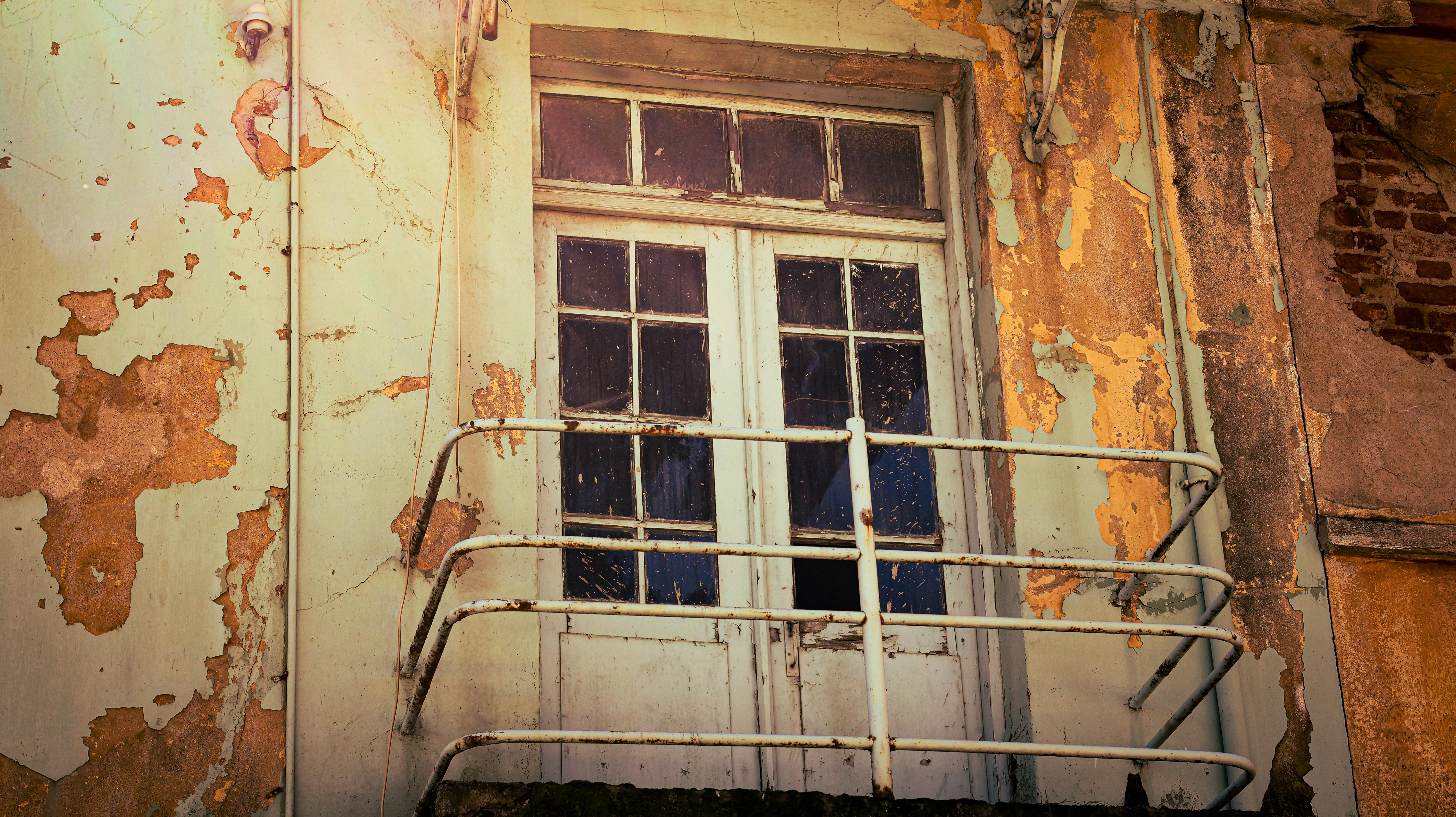 ingyenes Egy régi, viharvert homlokzat rozsdás erkéllyel és hámló festékkel, amely vintage hangulatot idéz. Stockfotó