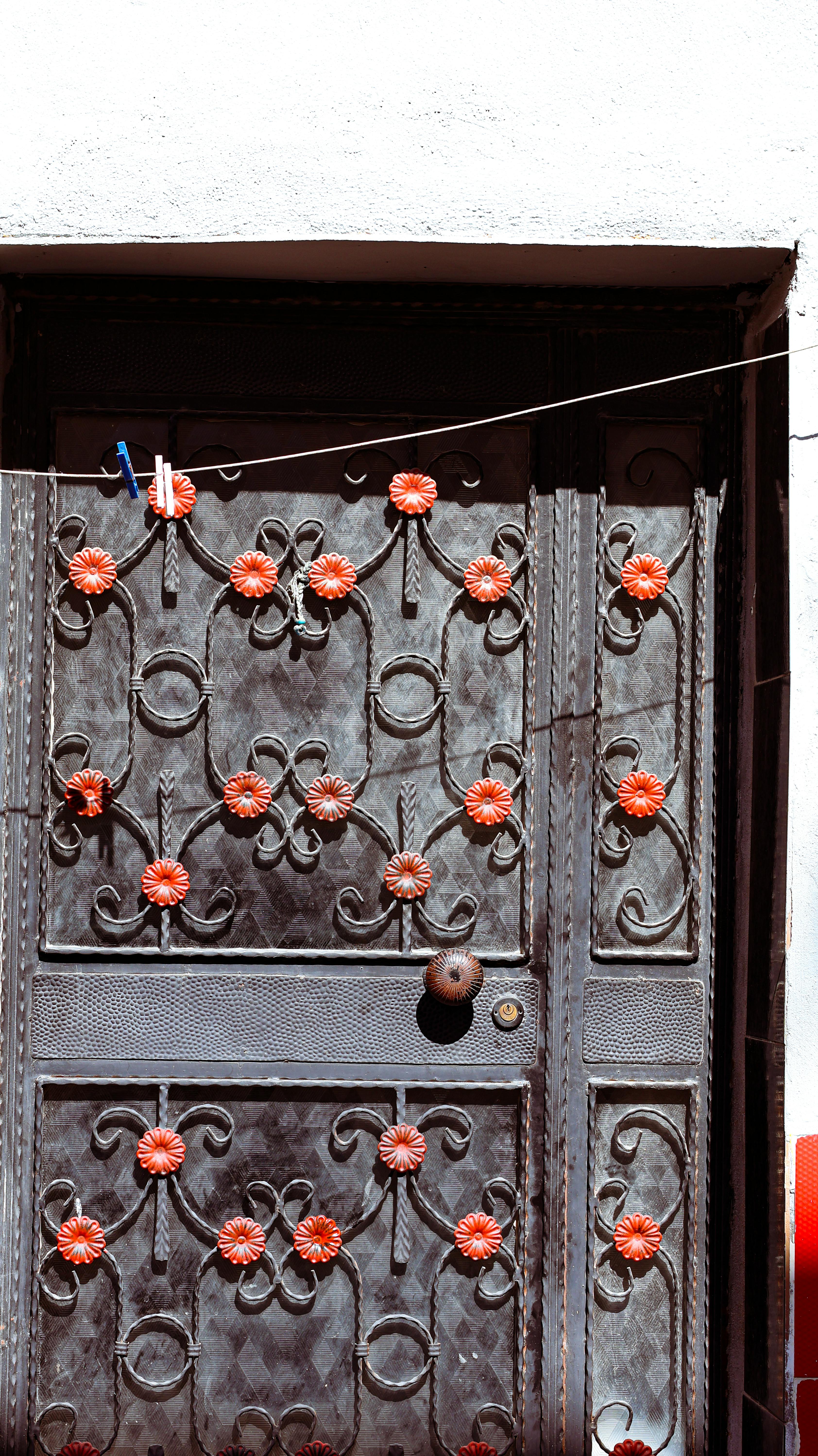 Zadarmo Rustikálne kovové dvere zdobené červenými kvetinovými dekoráciami pod jasným slnečným svetlom. Fotka z fotobanky