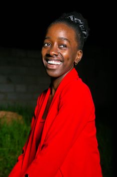 A cheerful woman in a vibrant red jacket smiling warmly against a dark background.