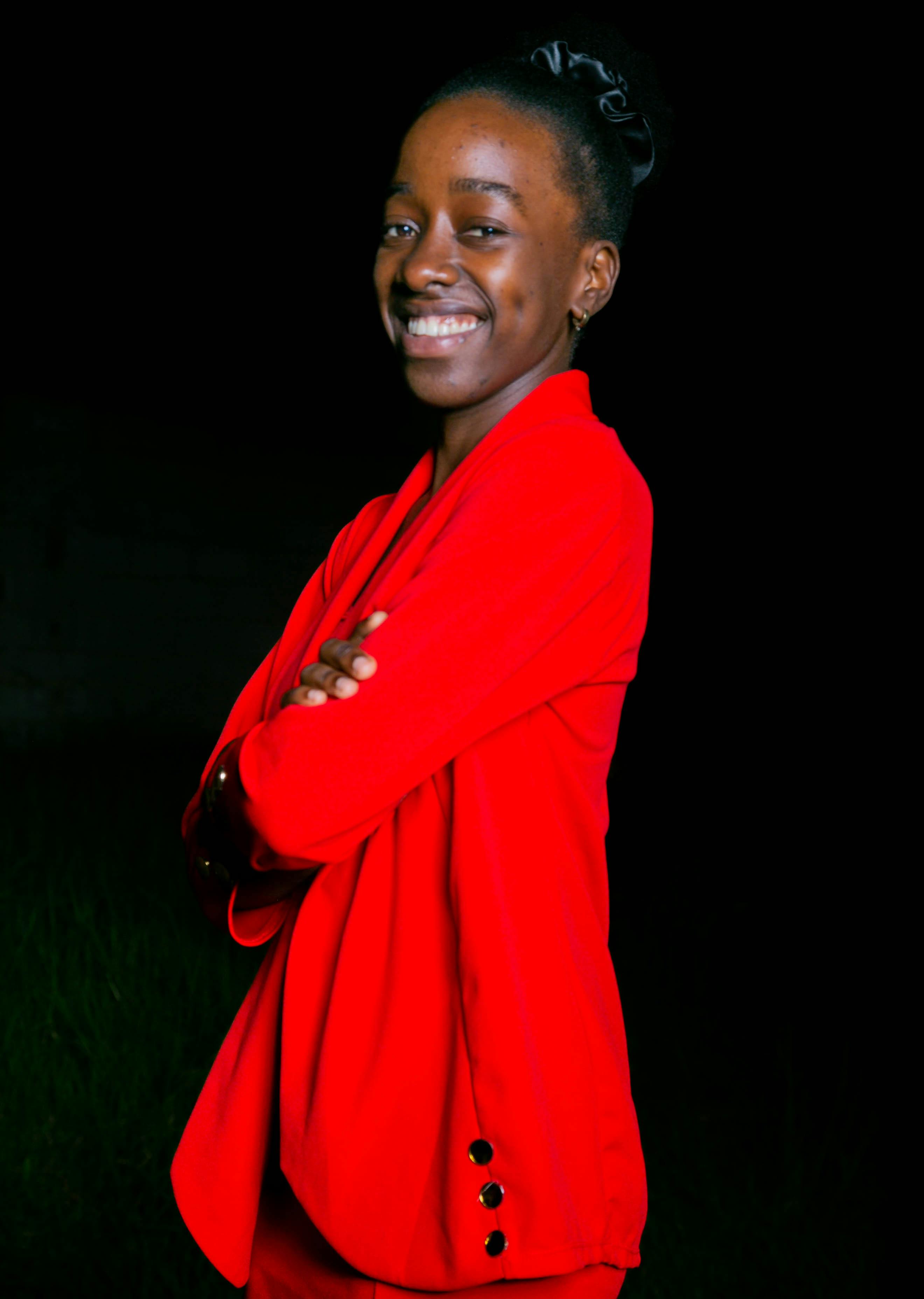 Miễn phí Người phụ nữ tươi cười trong chiếc áo khoác đỏ rực rỡ tạo dáng tự tin trước phông nền tối. Ảnh lưu trữ