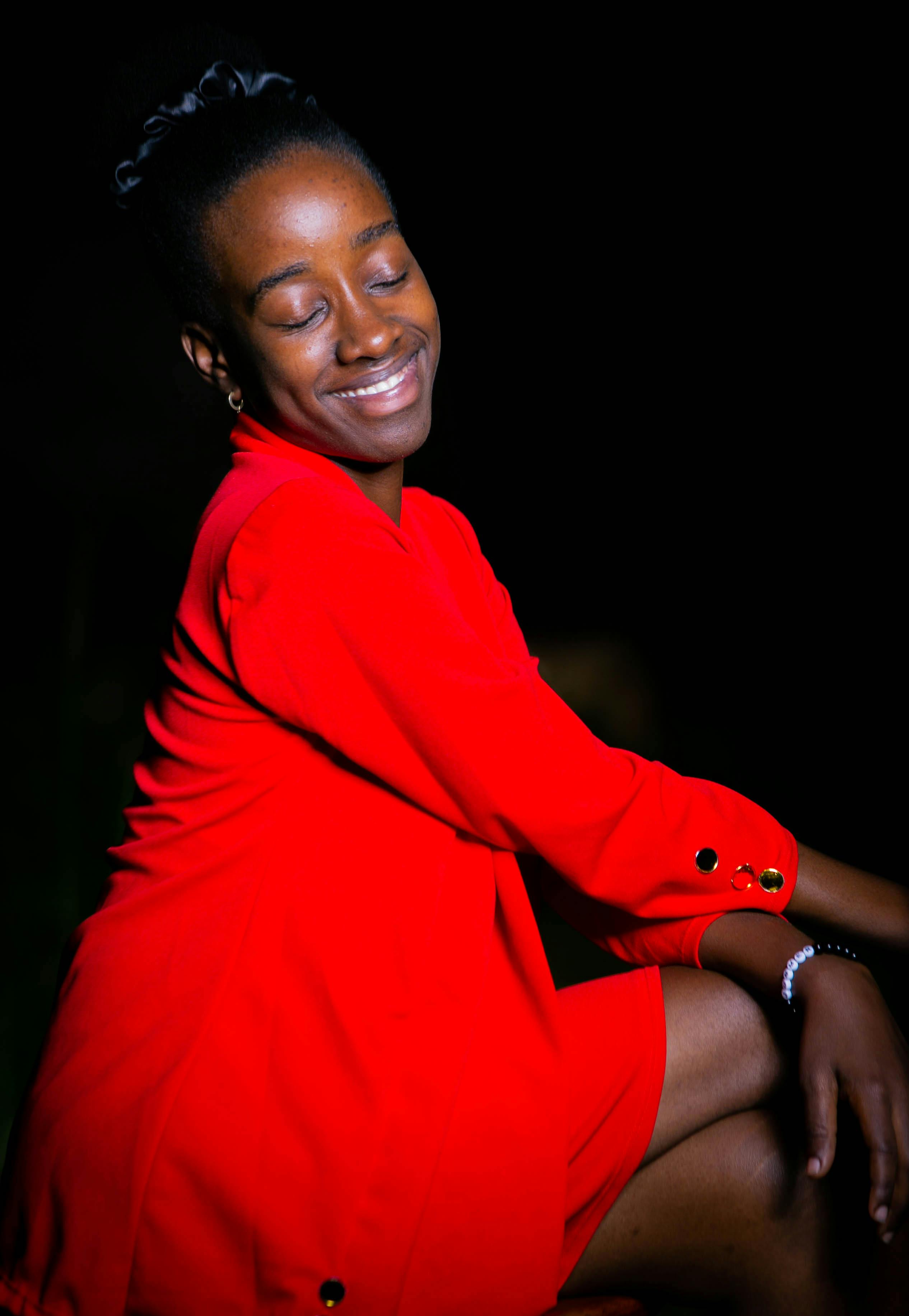 ฟรี ภาพถ่ายหญิงสาวผู้ร่าเริงในชุดเดรสสีแดง เปล่งประกายด้วยพลังบวกและสไตล์ที่โดดเด่นตัดกับฉากหลังสีเข้ม คลังภาพถ่าย