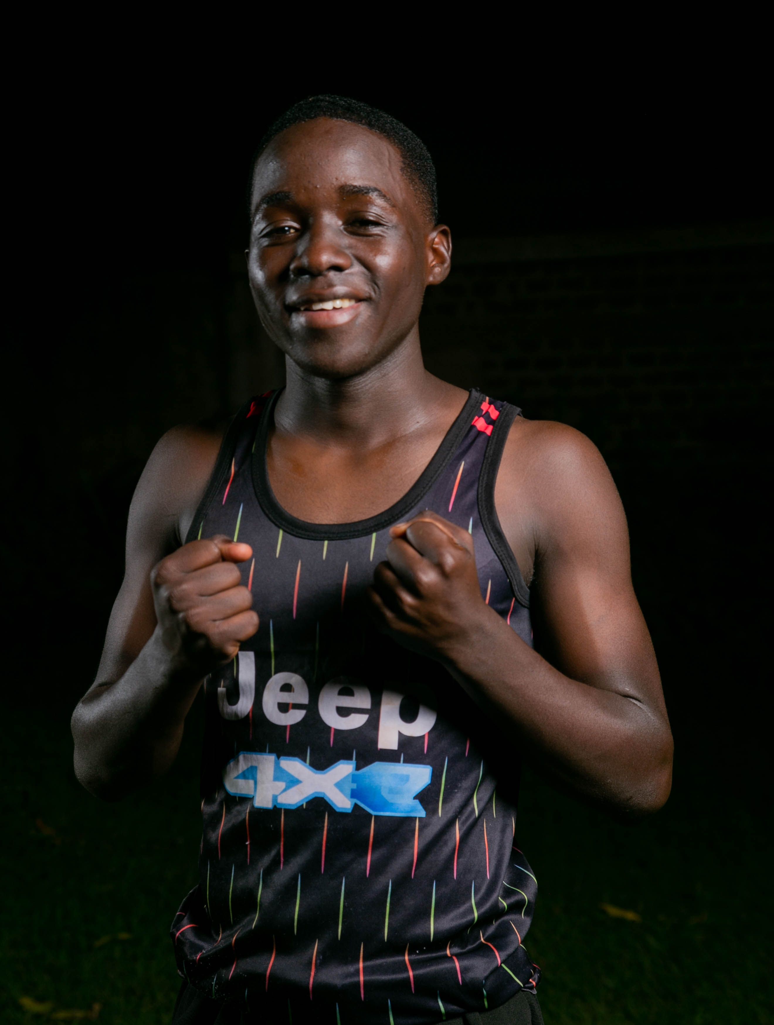 A young male boxer in a sleeveless shirt poses confidently at night outdoors.