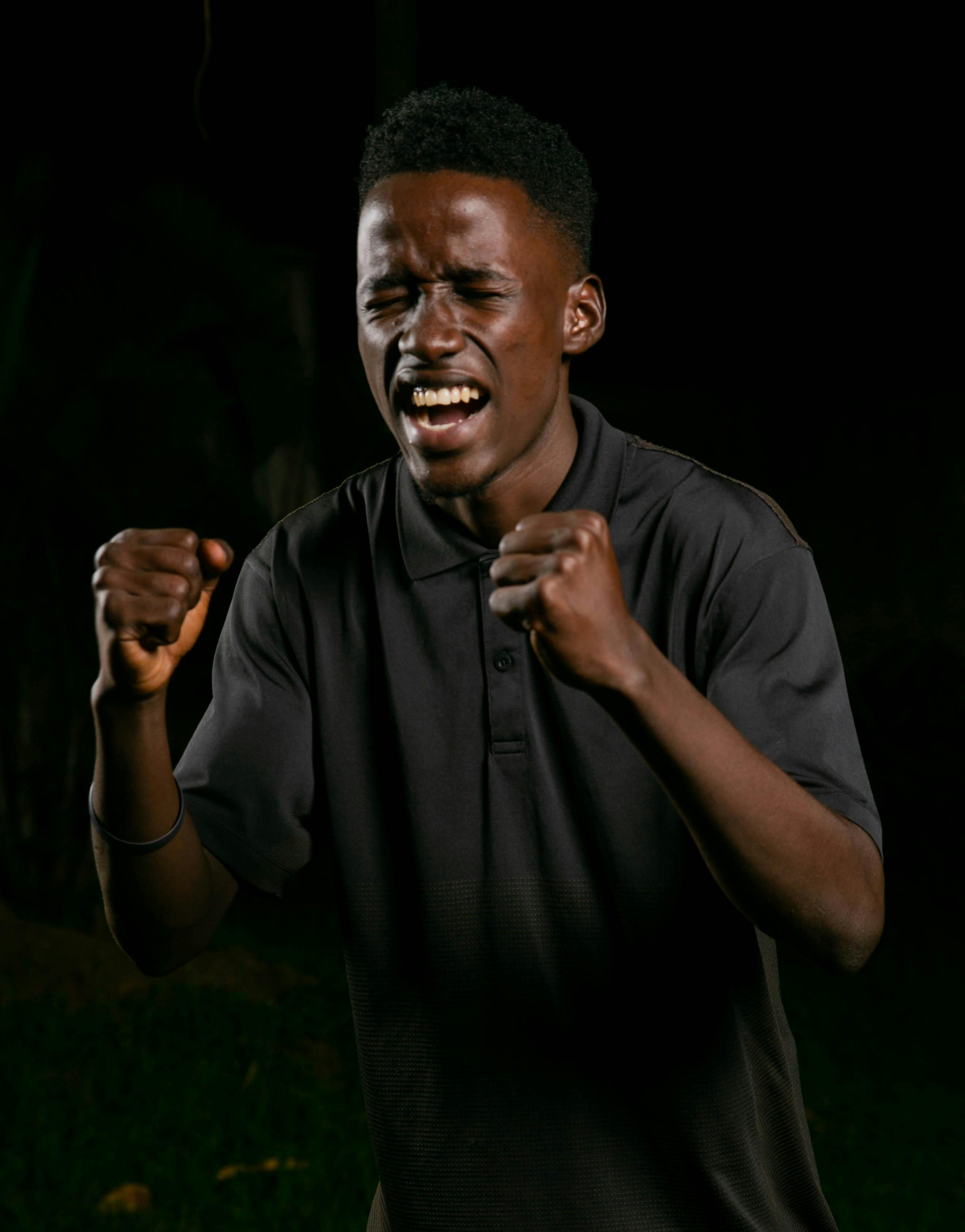 bezplatná Mladý muž radostně oslavuje vítězství v tmavém venkovním prostředí. Základová fotografie