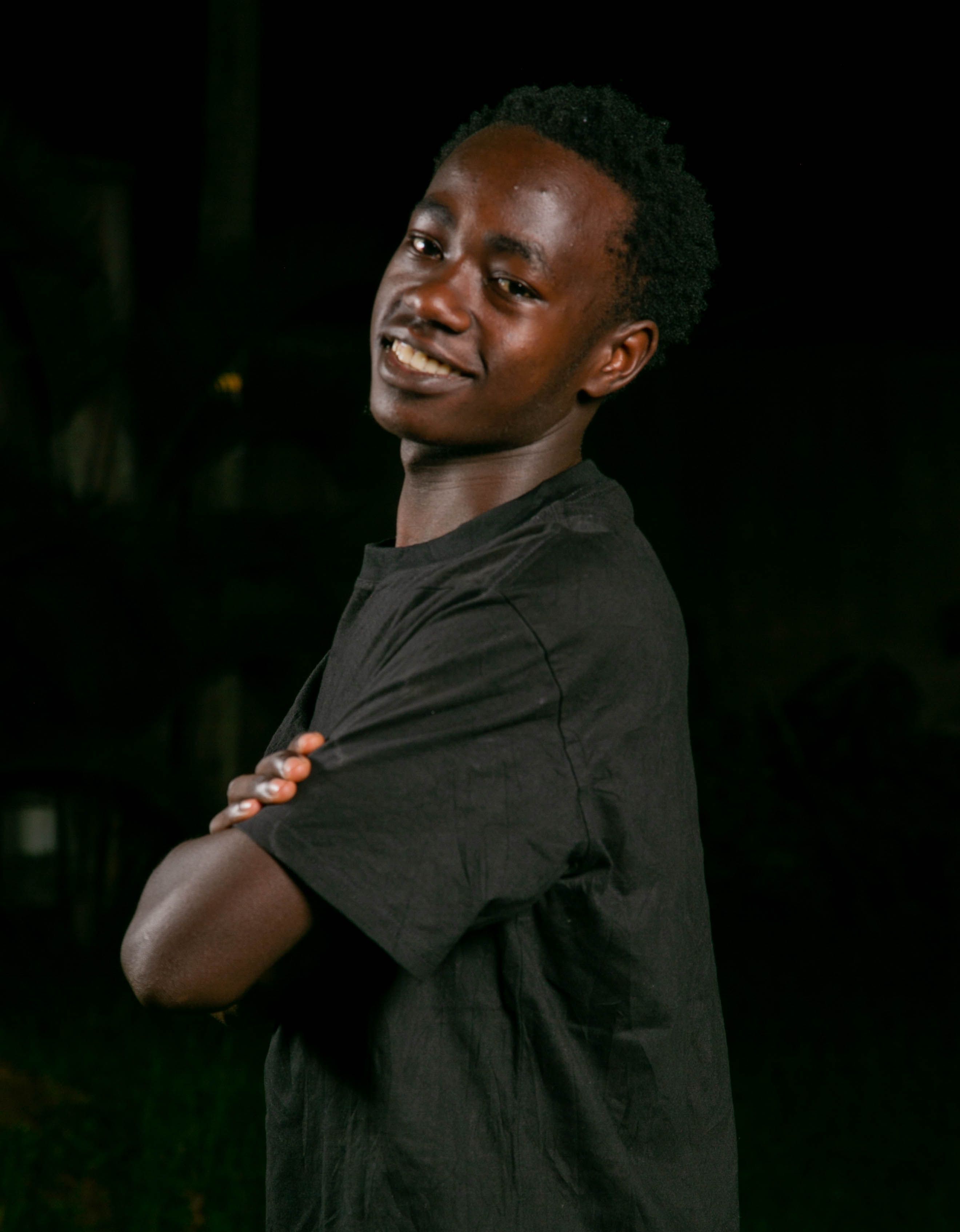 Young man standing confidently at night, smiling with arms crossed.