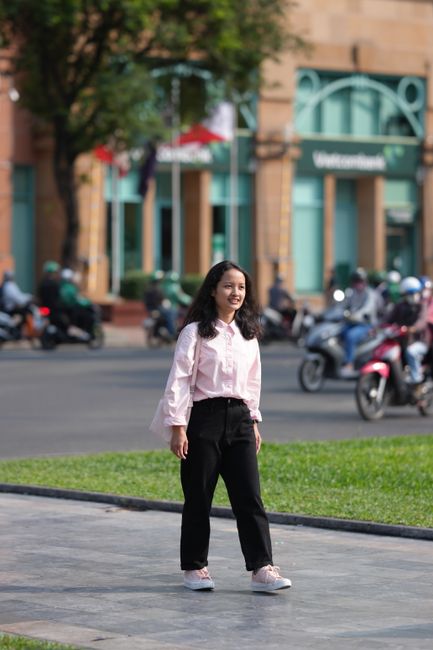 Young woman in casual attire smiling while walking on a bustling city street.