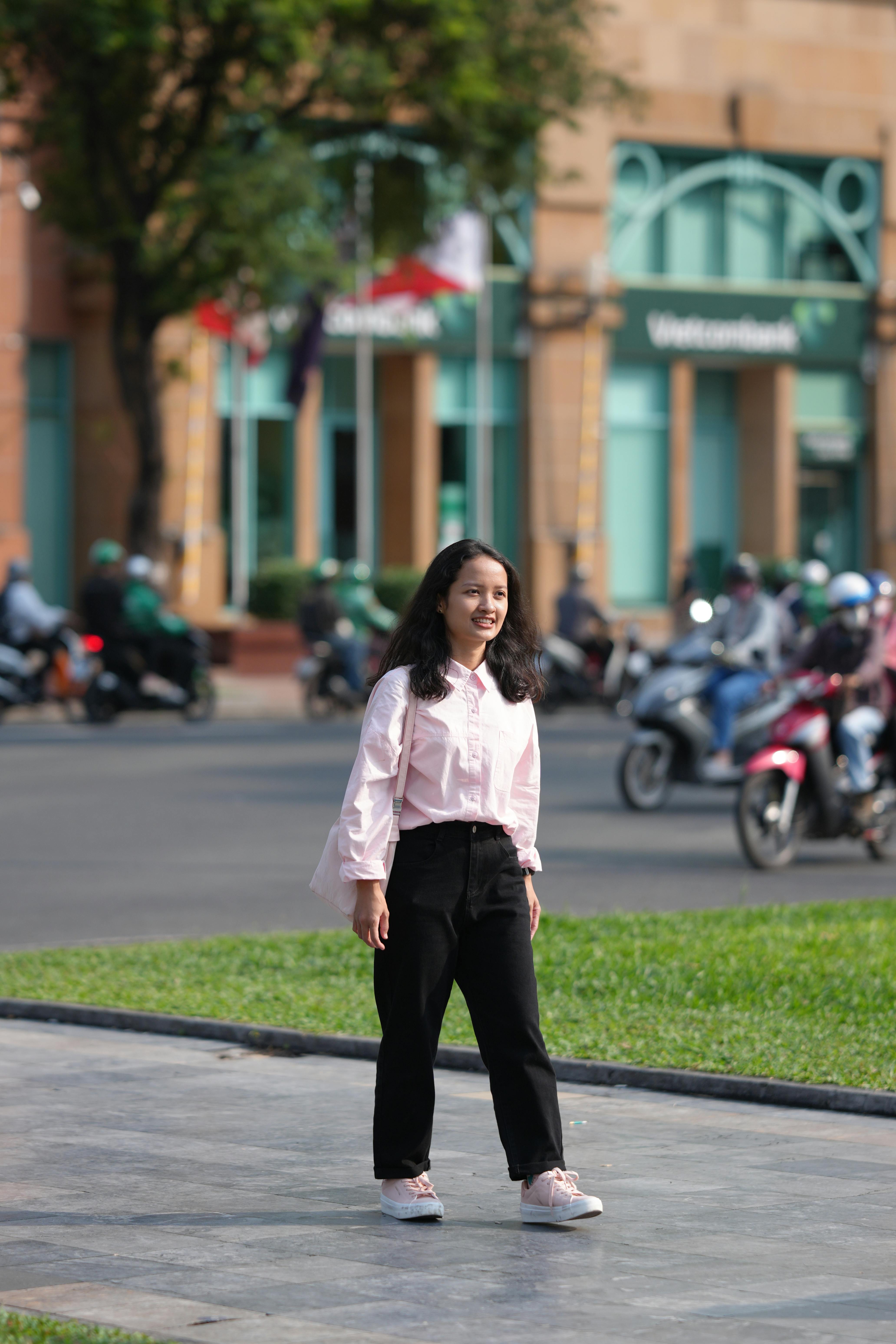 ingyenes Fiatal nő hétköznapi öltözékben mosolyogva sétál egy nyüzsgő városi utcán. Stockfotó