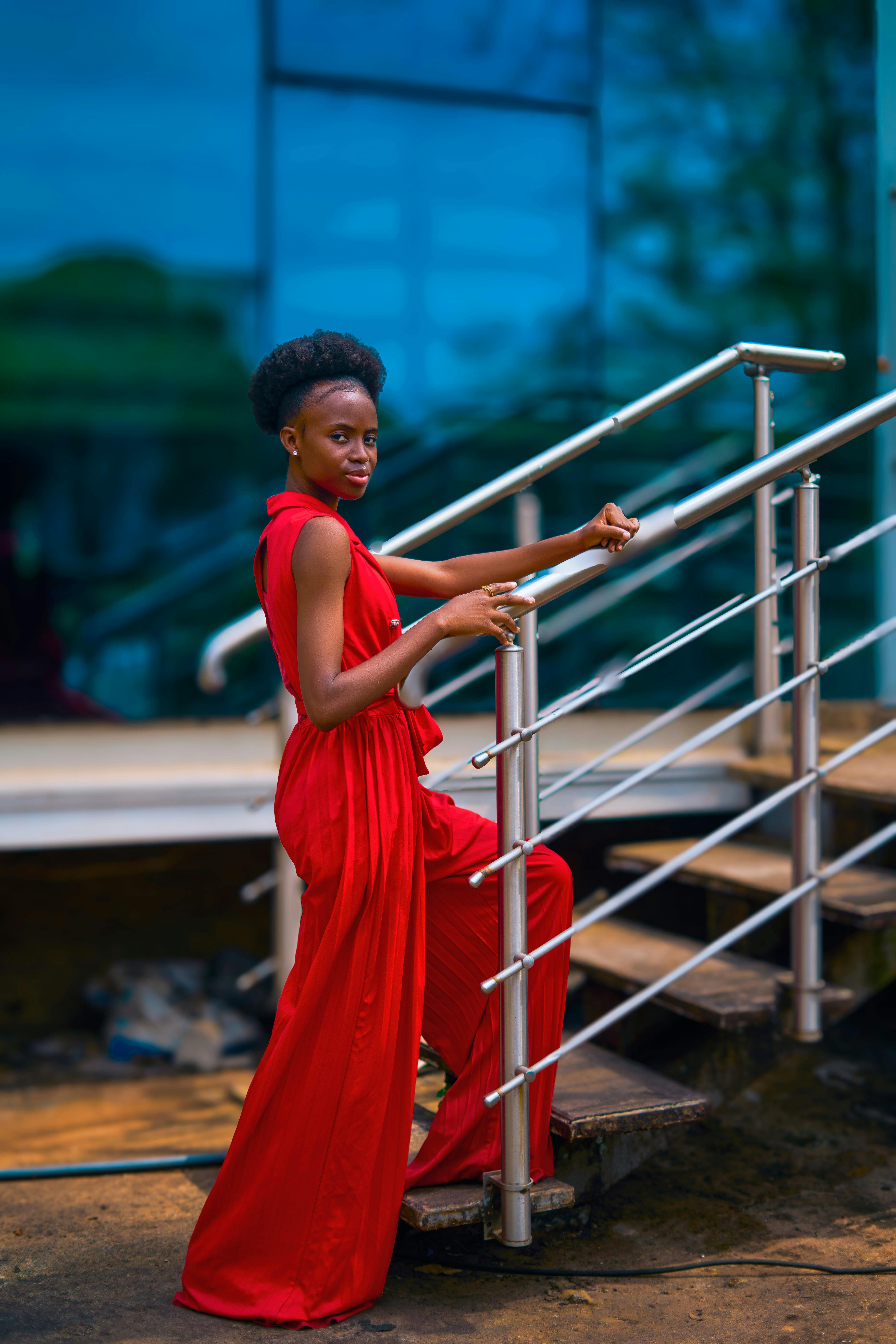 免費 一位身穿鮮豔紅色連身裙的優雅女士站在戶外樓梯上，拍攝了一張別緻的肖像照。 圖庫相片