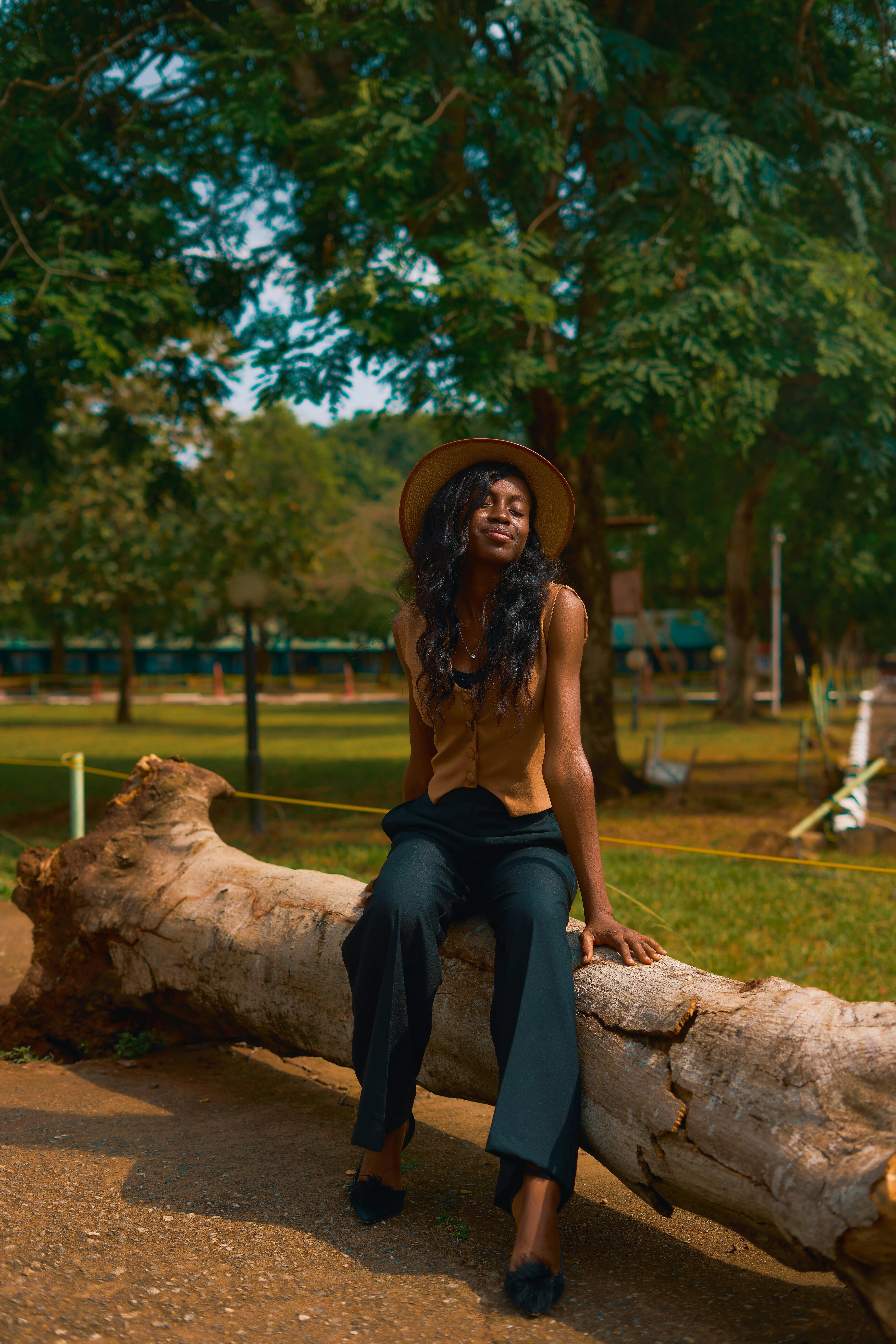 무료 한 여성이 라고스의 한 공원에서 쓰러진 나무 그루터기에 앉아 고요한 야외 환경을 즐기고 있다. 스톡 사진