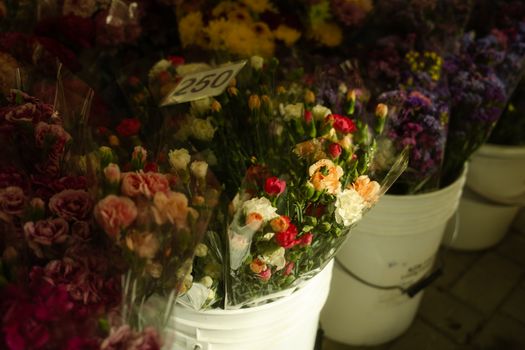 Colorful flower bouquets in white buckets at a market with price tag.