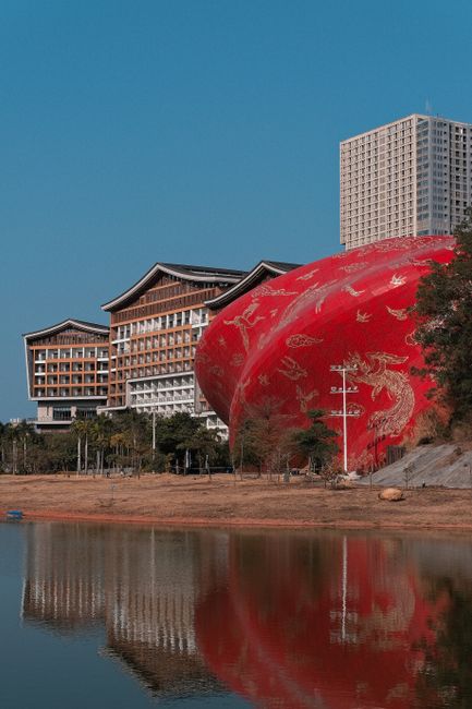 A scenic view of Sunac Guangzhou Grand Theatre with its striking red facade reflecting in the water under a clear blue sky.