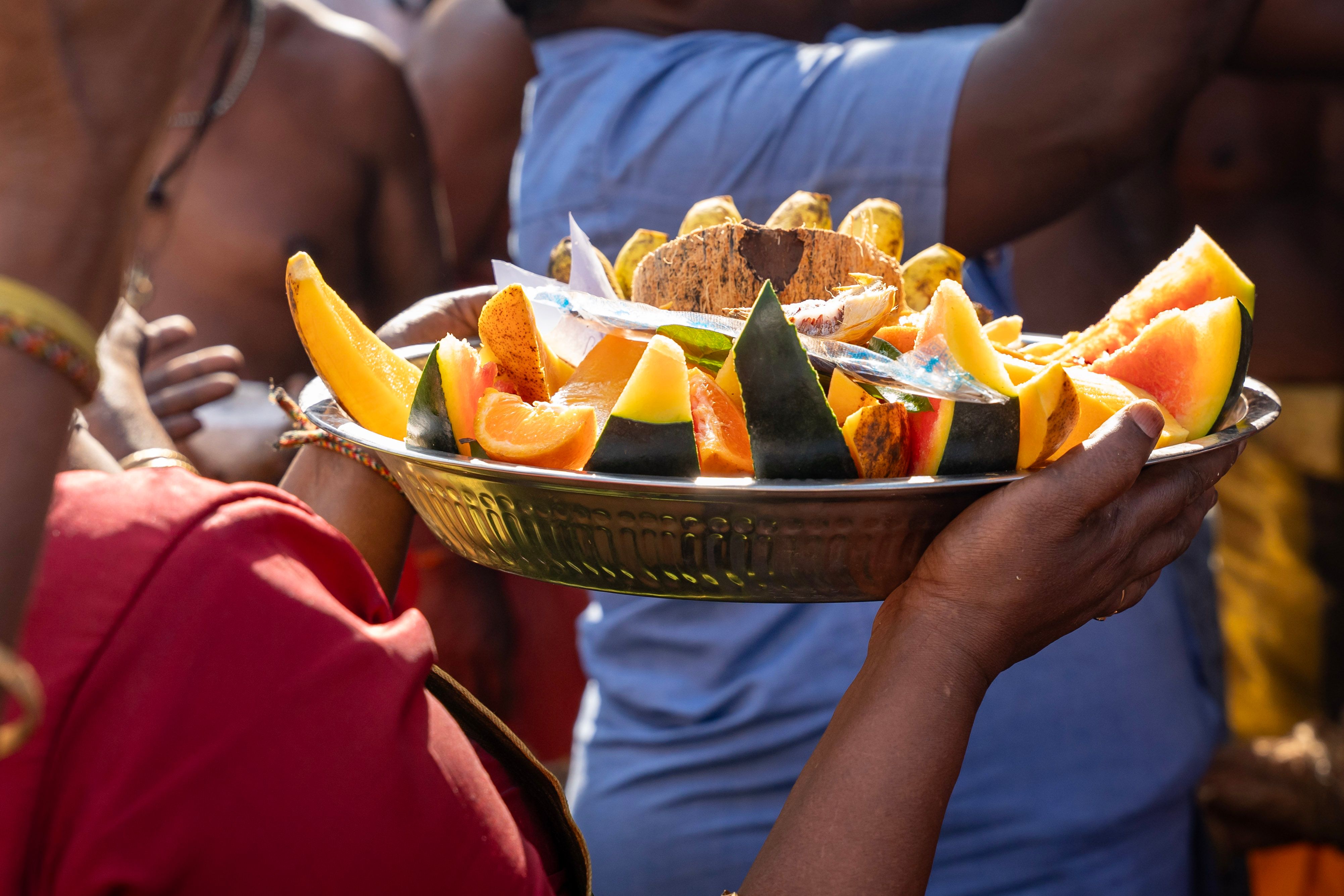Close-up of hands offering a bowl of fresh, colorful local fruit to a traveler