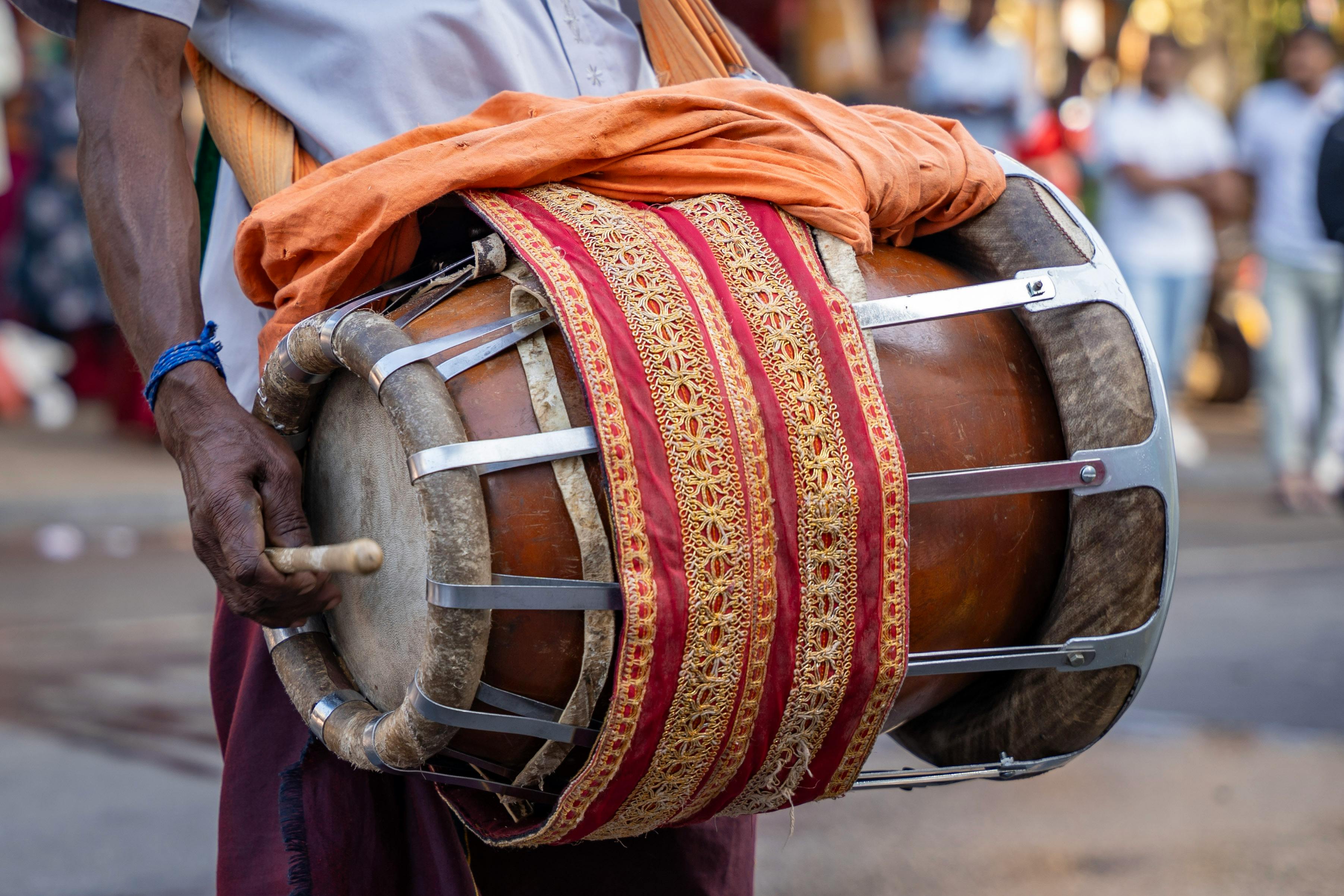 A musician plays a traditional Indian drum during a bustling outdoor festival.