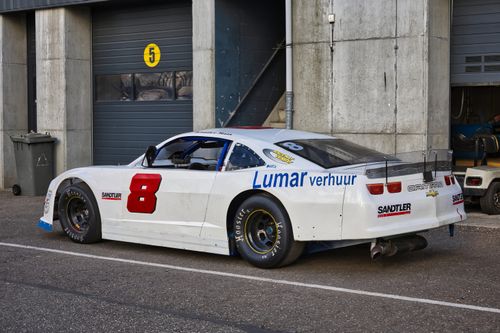 Free A white stock car parked outside a motorsport garage, ready for race day. Stock Photo