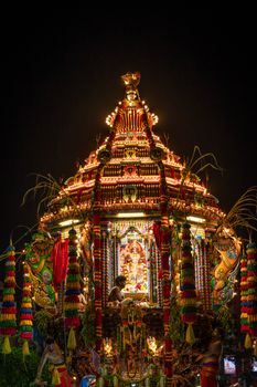 An ornate, illuminated chariot at a Hindu festival parade during nighttime.