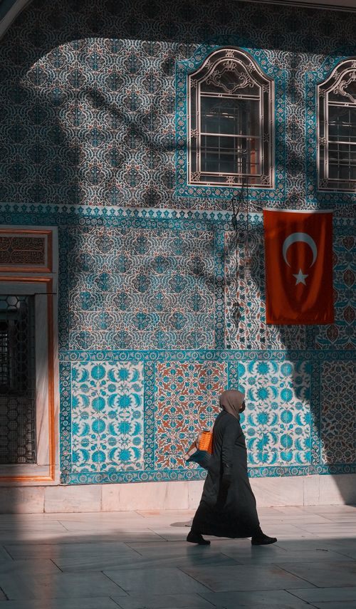 Free A woman walks past a beautifully tiled wall with Turkish flag in Istanbul, Türkiye. Stock Photo