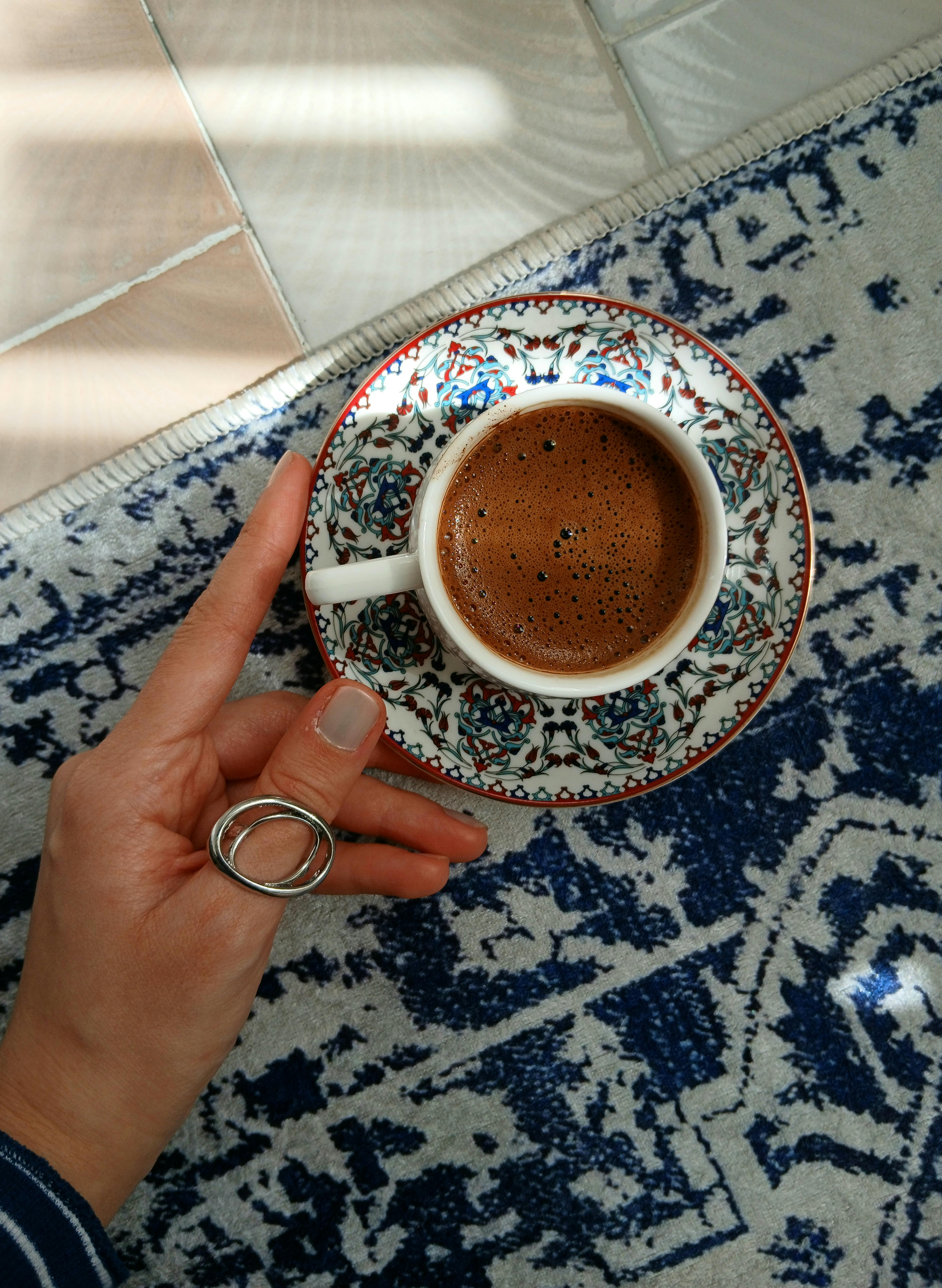 Hand holding a traditional Turkish coffee cup with ornate saucer on a blue rug.