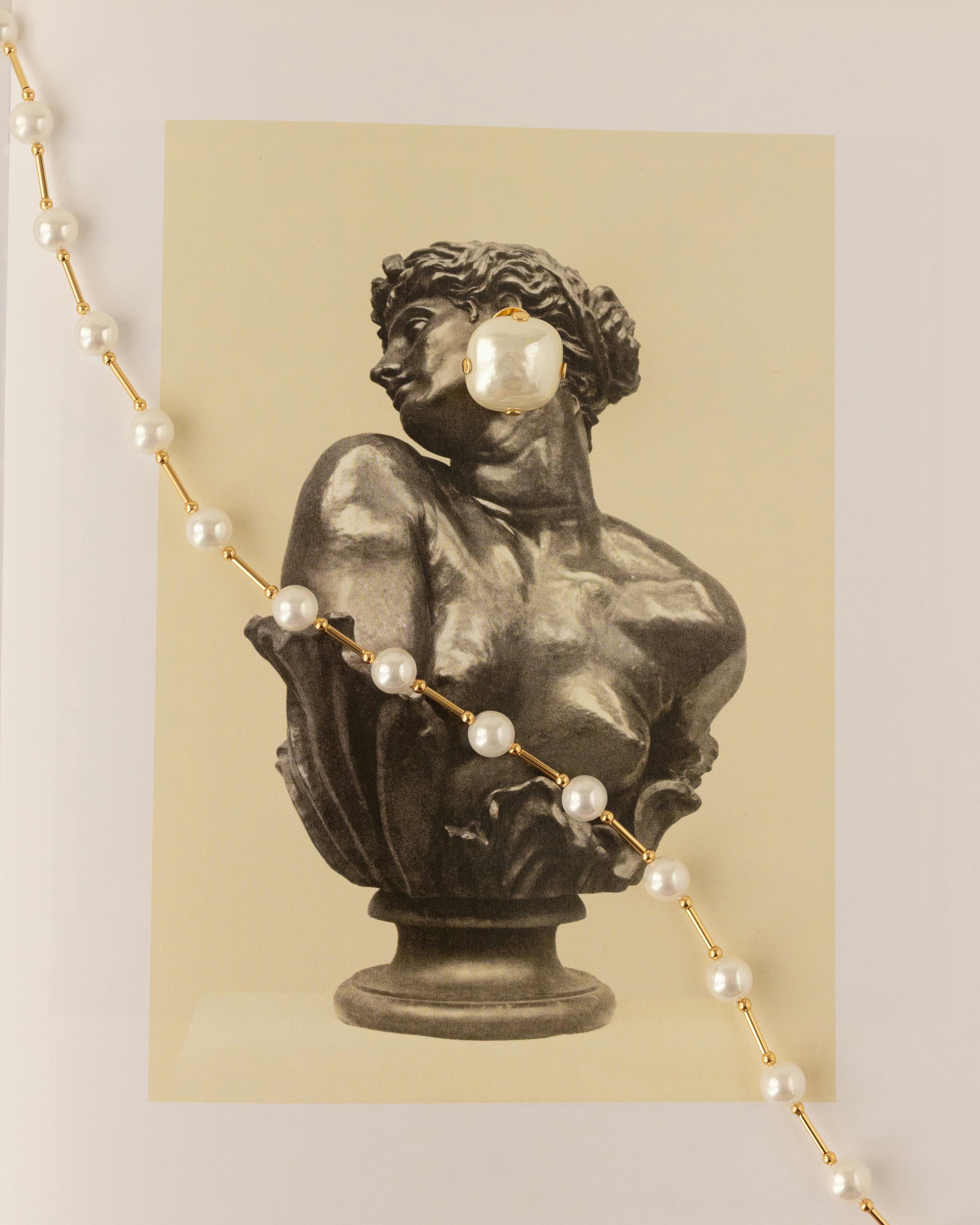 무료 흑백 조각 예술과 현대적인 진주 목걸이가 대비를 이룬다. 스톡 사진