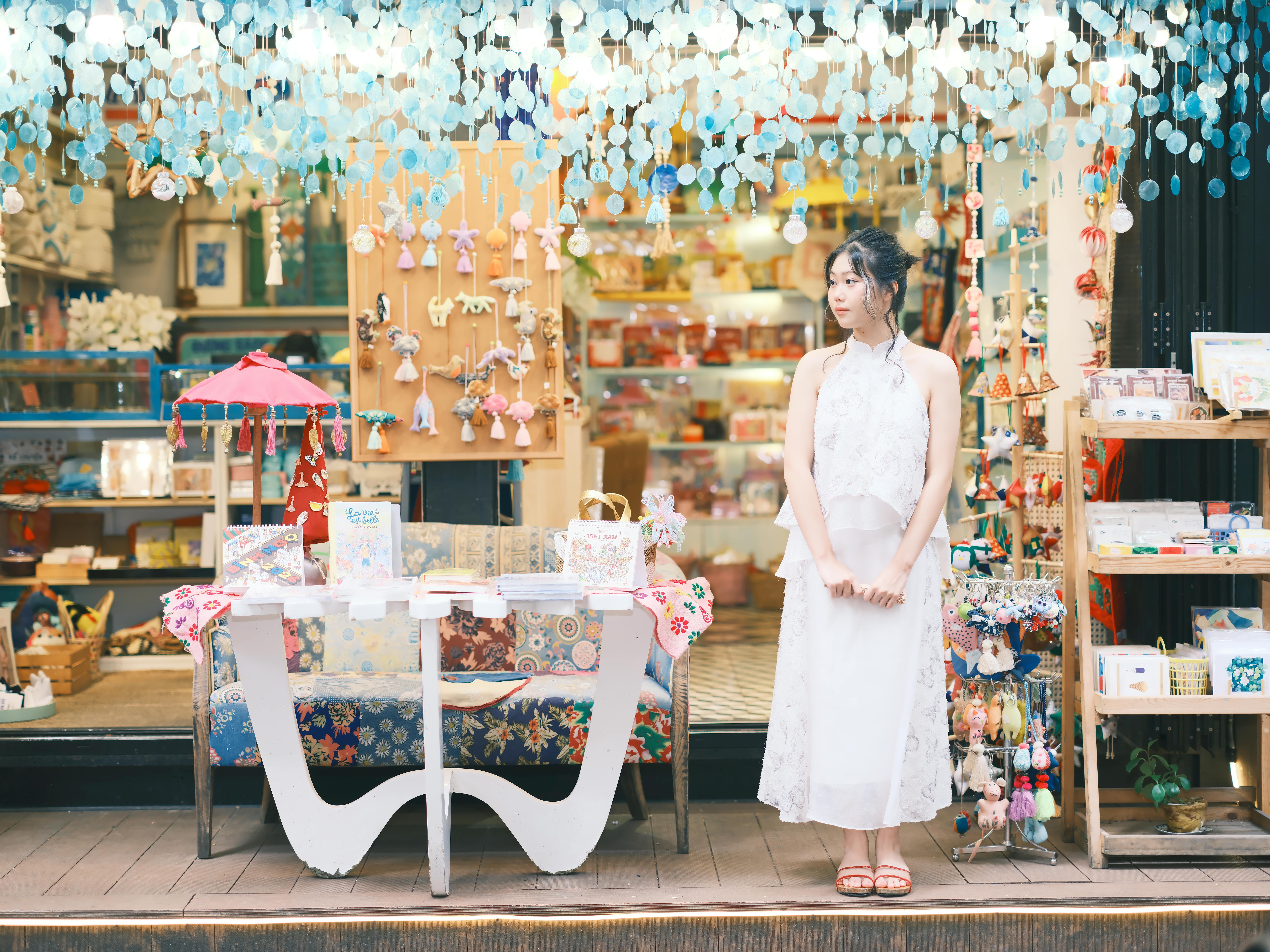 免费 一位身穿白色连衣裙的时尚女士站在一家古朴多彩的礼品店外。 素材图片