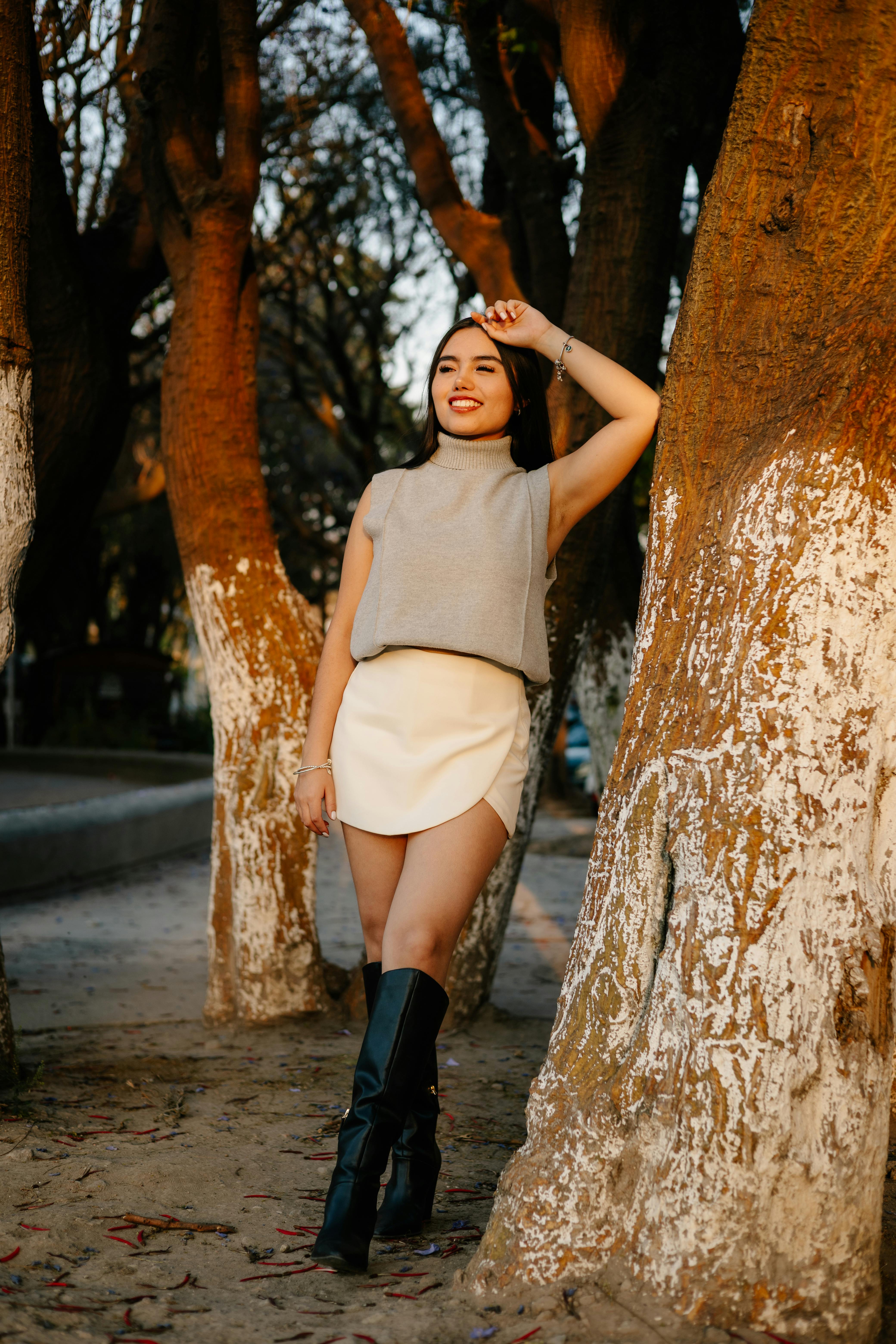 免费 白天，一位身着时尚服装的女士在公园里，站在彩绘树木旁摆姿势拍照。 素材图片