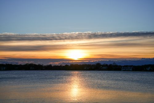 Free Capture of a peaceful sunrise over a calm lake with dramatic sky colors reflecting on the water. Stock Photo