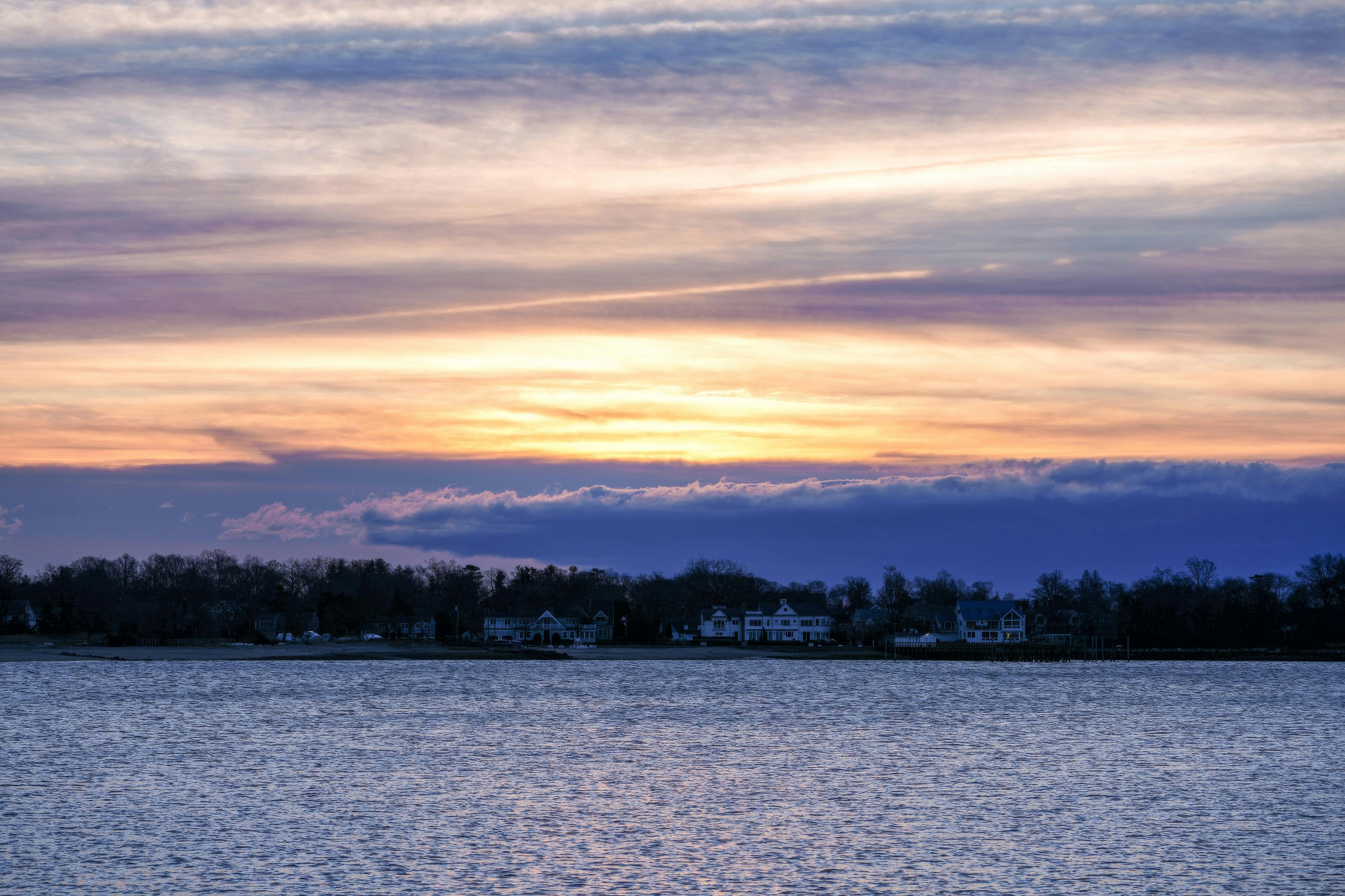 免費 夕陽西下，映照著平靜的湖面和周圍的房屋，景色優美，營造出寧靜祥和的氛圍。 圖庫相片