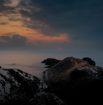 Serene view of dramatic sunset over the ocean with rocky foreground.
