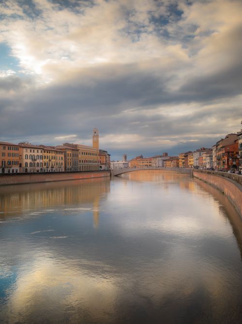Free Beautiful sunset view over the Arno River in Pisa with reflections and historic buildings. Stock Photo