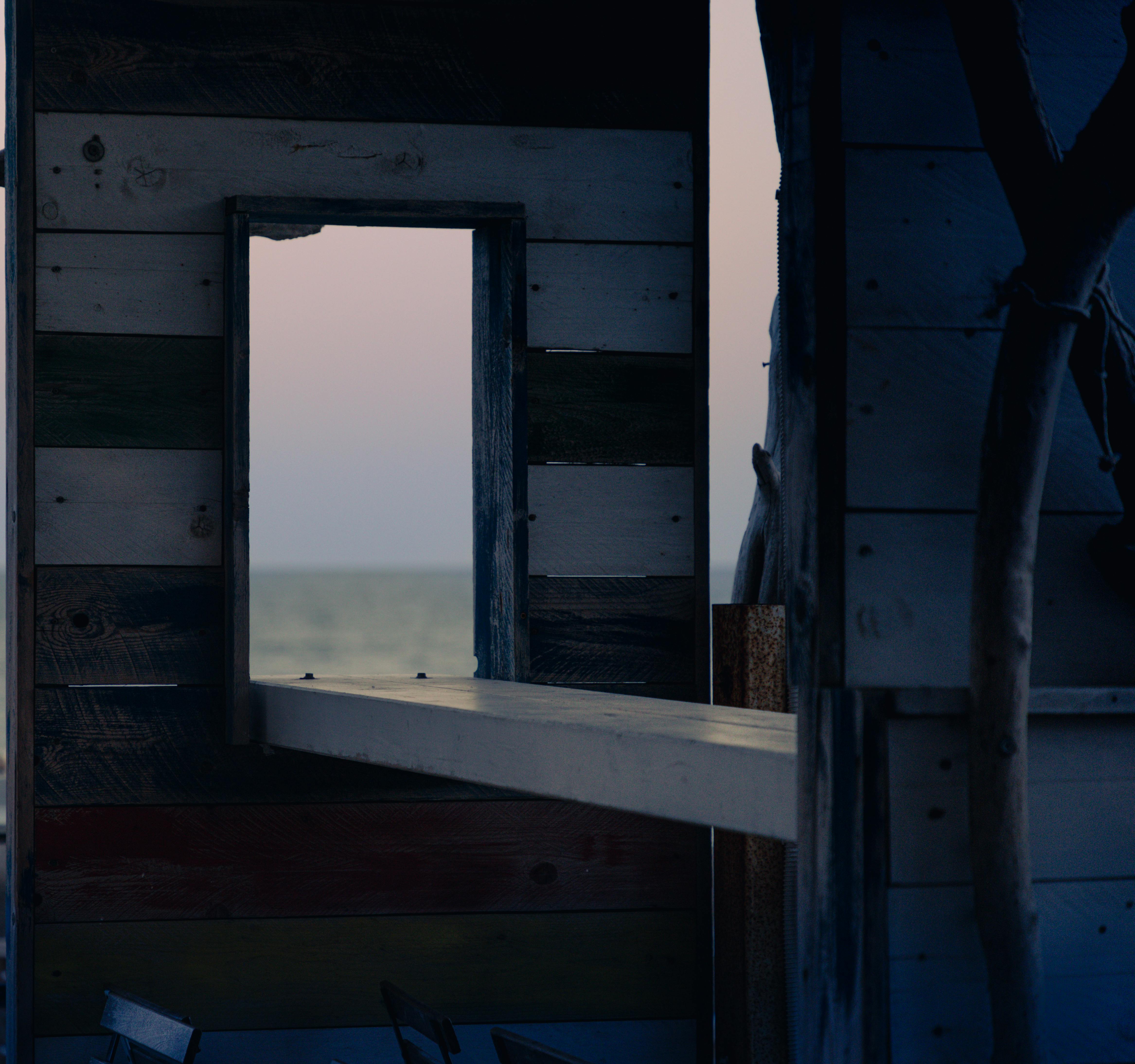 Безкоштовне Спокійний краєвид узбережжя через вікно дерев'яної конструкції у сутінках. стокове фото