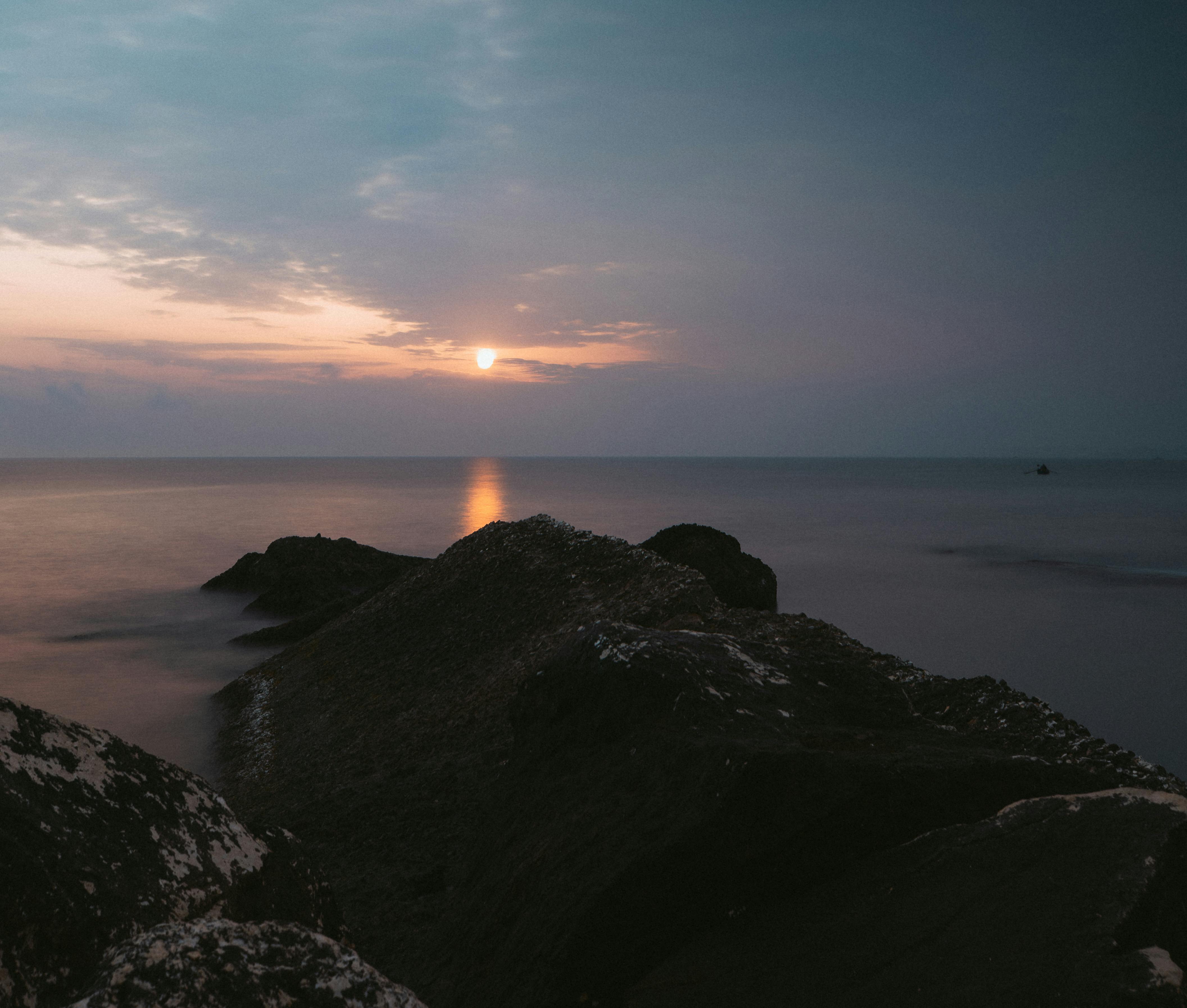 Zadarmo Pokojný výhľad na západ slnka nad oceánom so skalnatým pobrežím, ideálny pre pokojnú atmosféru. Fotka z fotobanky