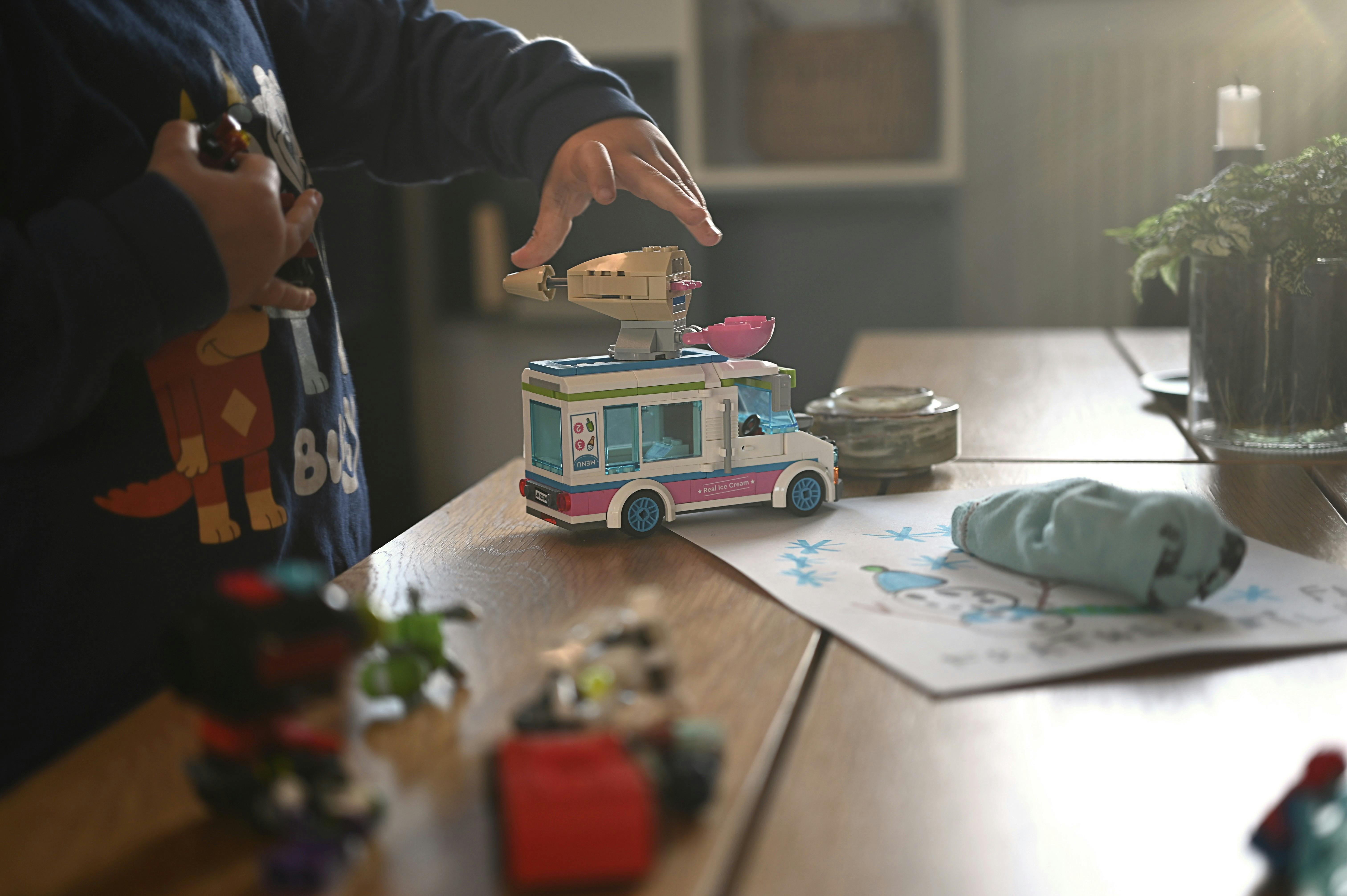 ingyenes Egy gyerek egy játék furgonnal játszik egy jól megvilágított asztalon bent, színes rajzok és akciófigurák között. Stockfotó