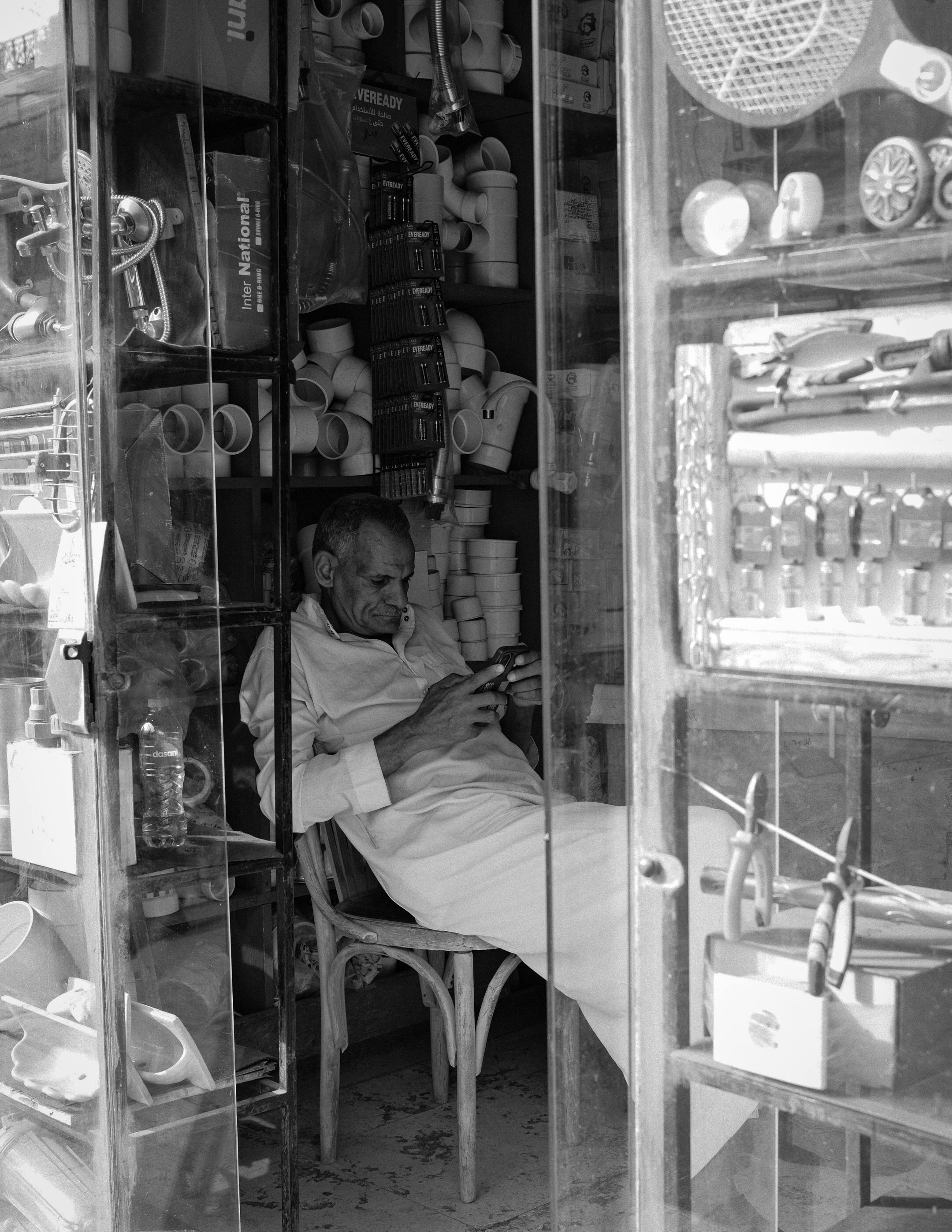 ฟรี ภาพถ่ายขาวดำของชายคนหนึ่งในร้านขายอุปกรณ์ฮาร์ดแวร์ กำลังพักผ่อนพร้อมกับโทรศัพท์มือถือ คลังภาพถ่าย