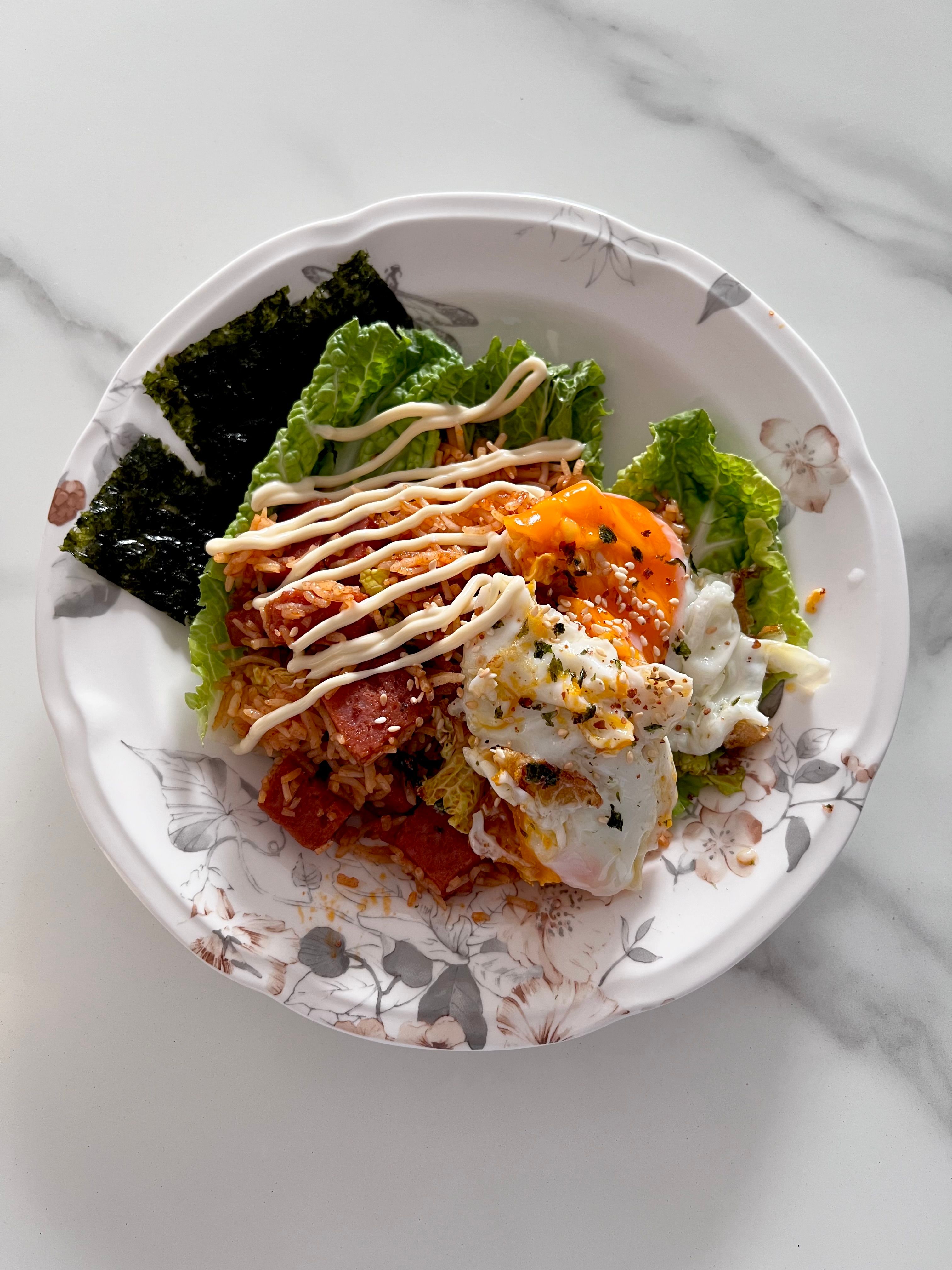 Tasty Korean bibimbap with poached egg, seaweed, and vegetables served on a floral plate.