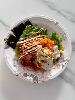 Tasty Korean bibimbap with poached egg, seaweed, and vegetables served on a floral plate.