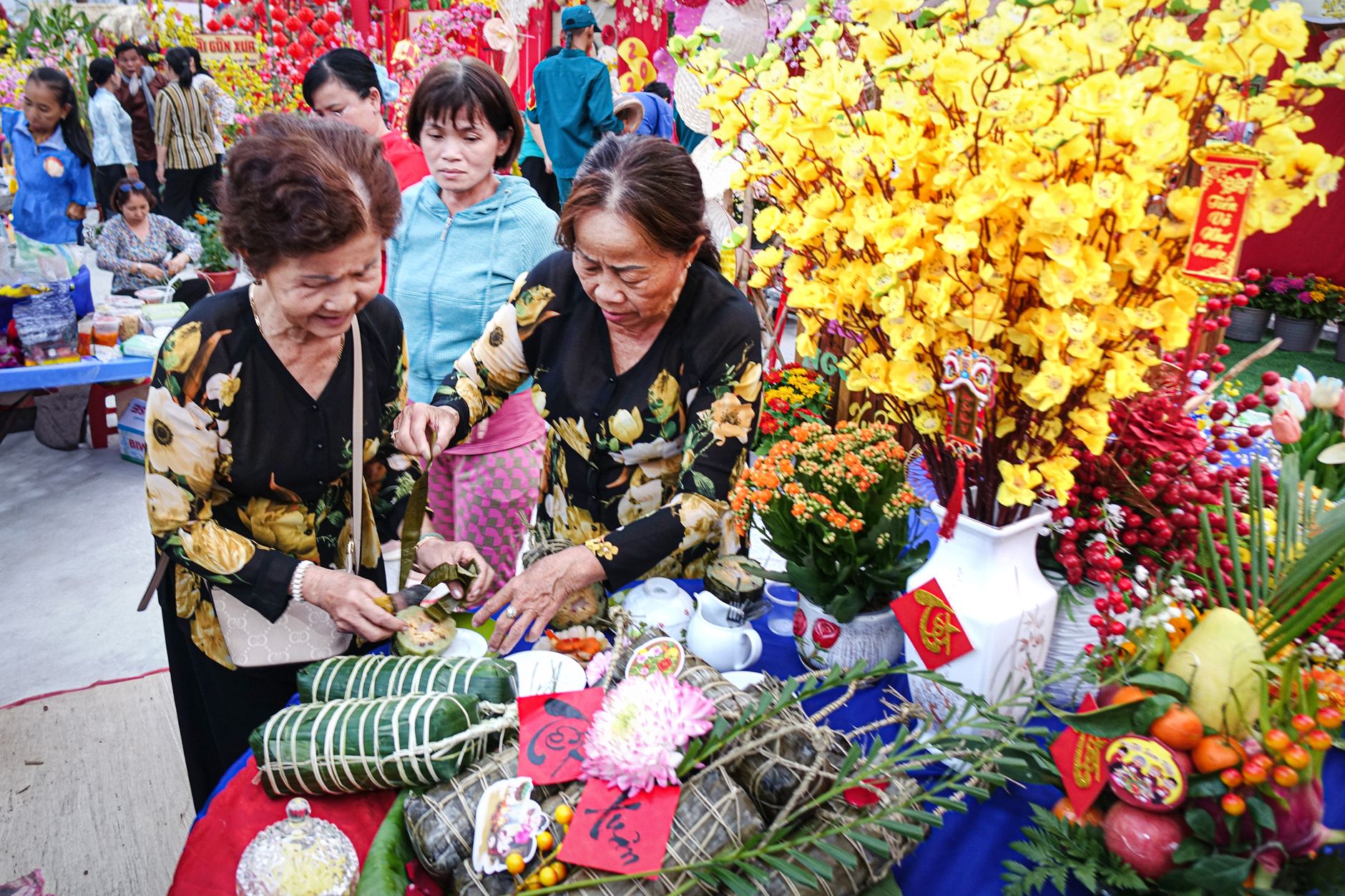 Elderly women preparing traditional foods at a vibrant Vietnamese Tet festival with flowers.